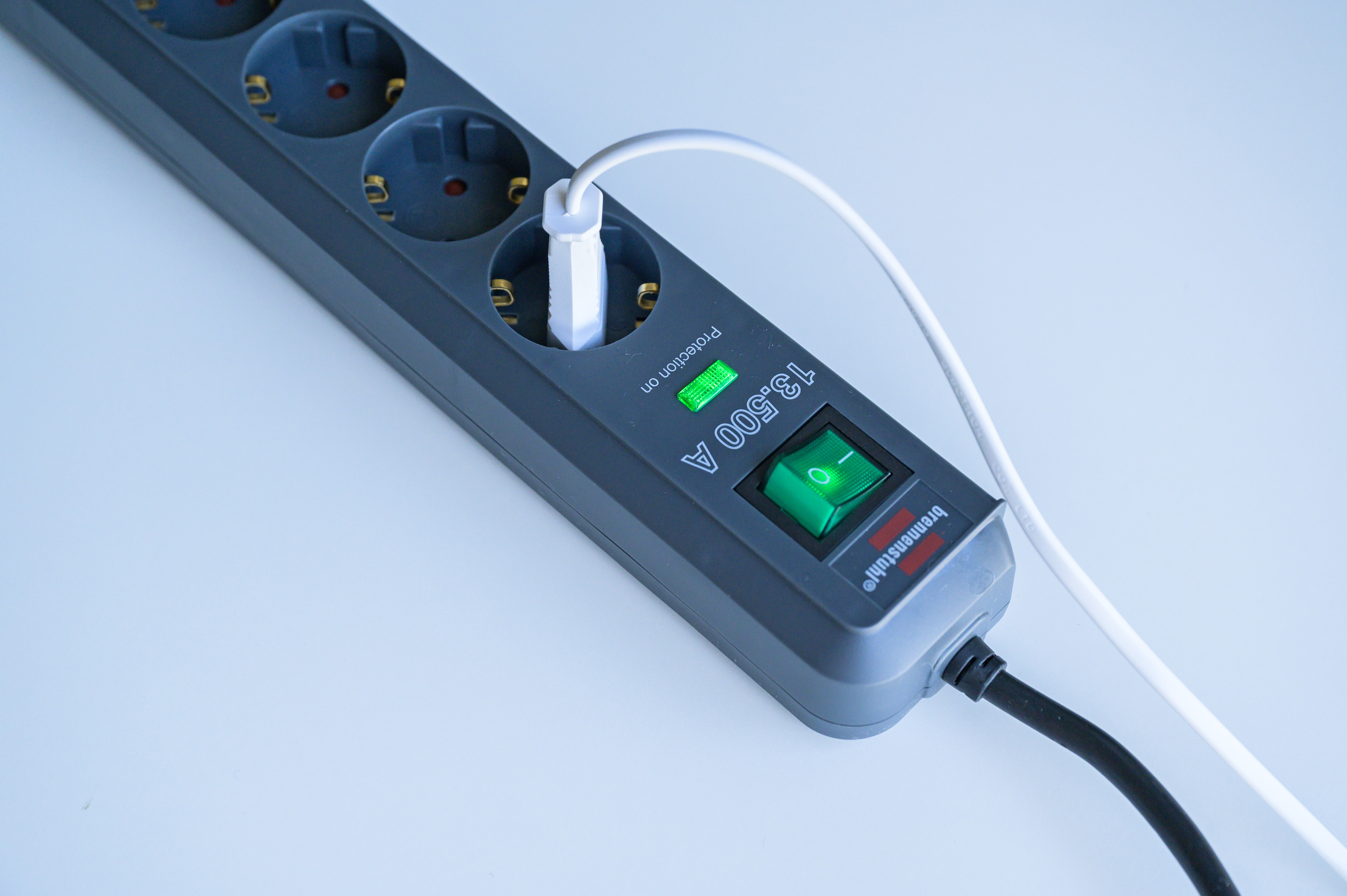 Eine graue Mehrfachsteckdose mit eingeschaltetem grünen Schalter und einem eingesteckten weißen Kabel.