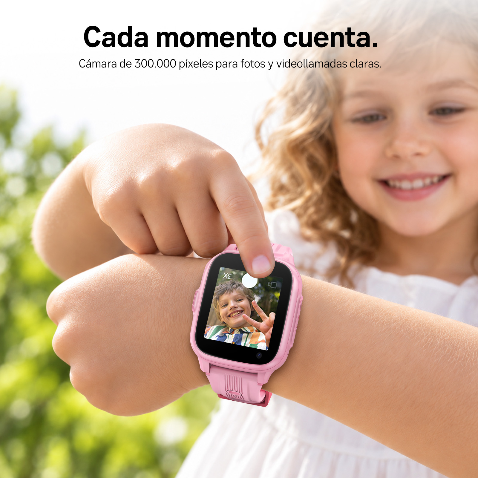Una niña sonriente señala un reloj inteligente rosa con cámara en su muñeca.