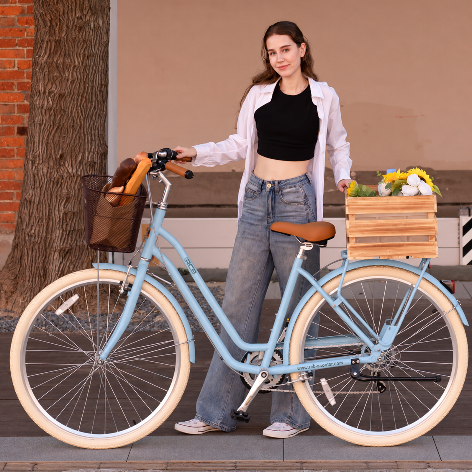 Eine Frau in weißem Hemd und Jeans steht neben einem hellblauen Fahrrad mit Korb und Blumen.