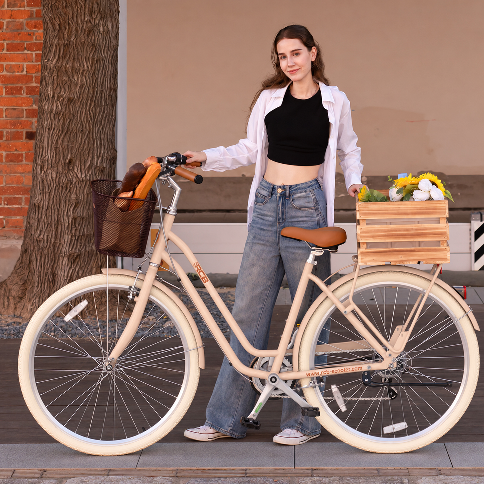 Eine junge Frau in Jeans und weißem Hemd steht neben einem cremefarbenen Fahrrad mit Brot und Blumen.