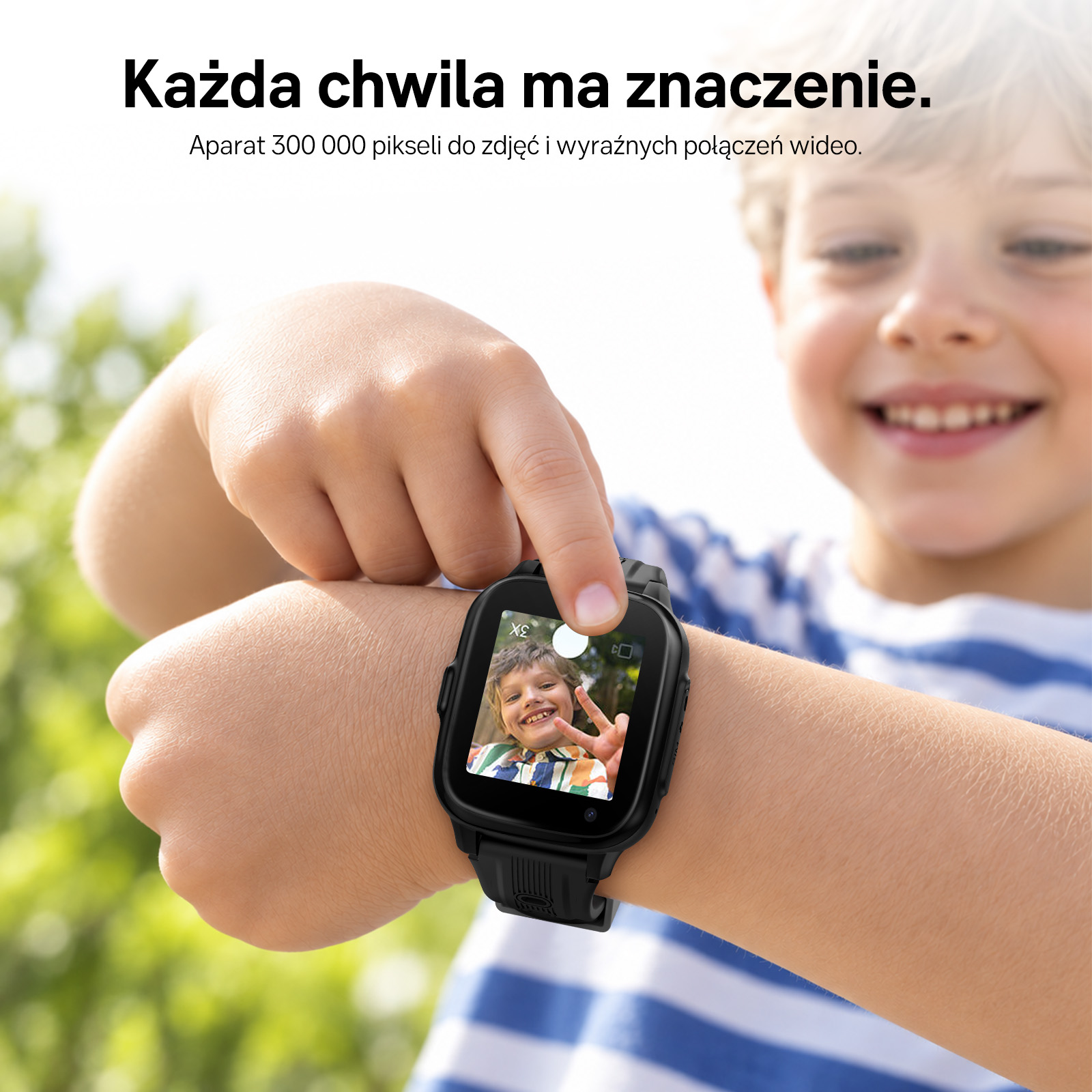 Uśmiechnięty chłopiec w pasiastej koszulce nosi smartwatch i dotyka jego ekranu.