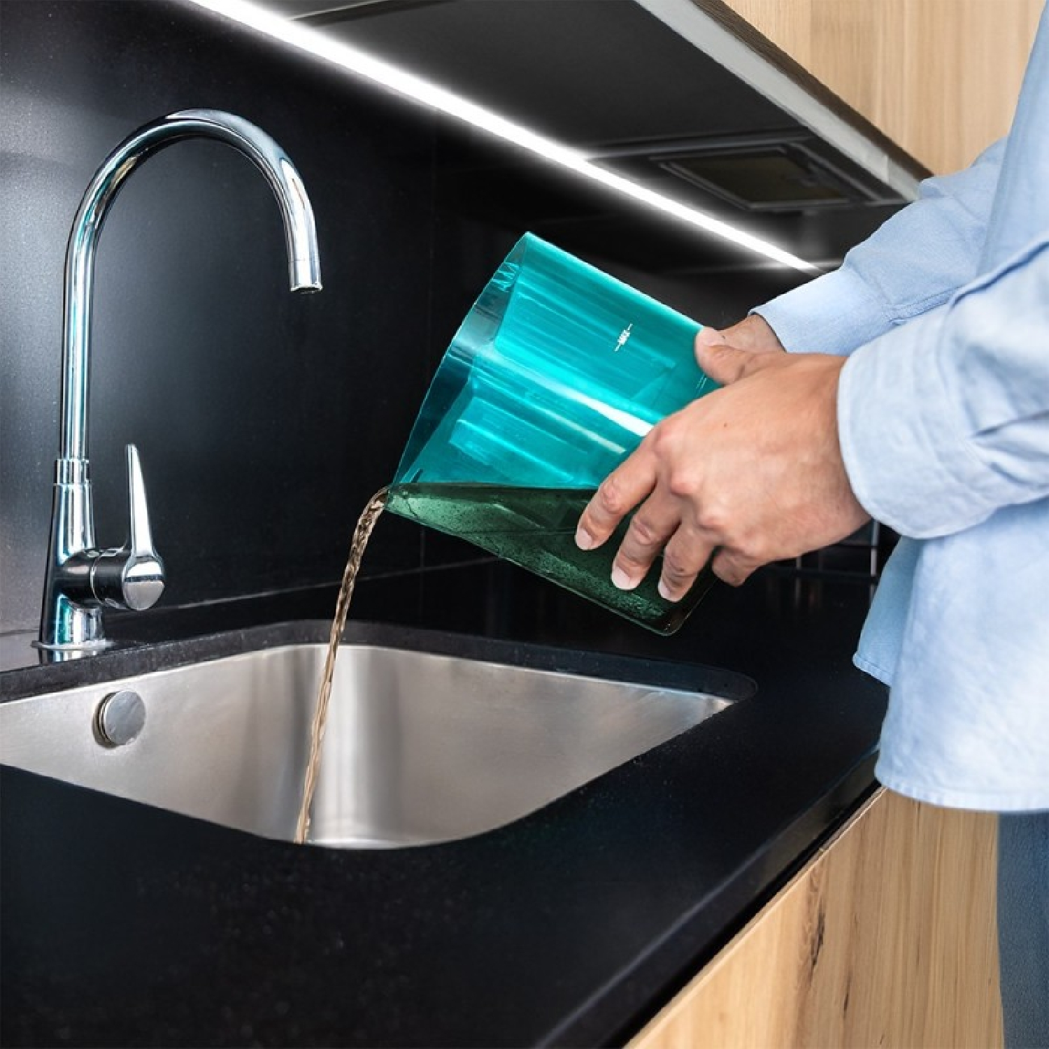 Una persona versa acqua da una brocca blu in un lavello da cucina in acciaio inossidabile.