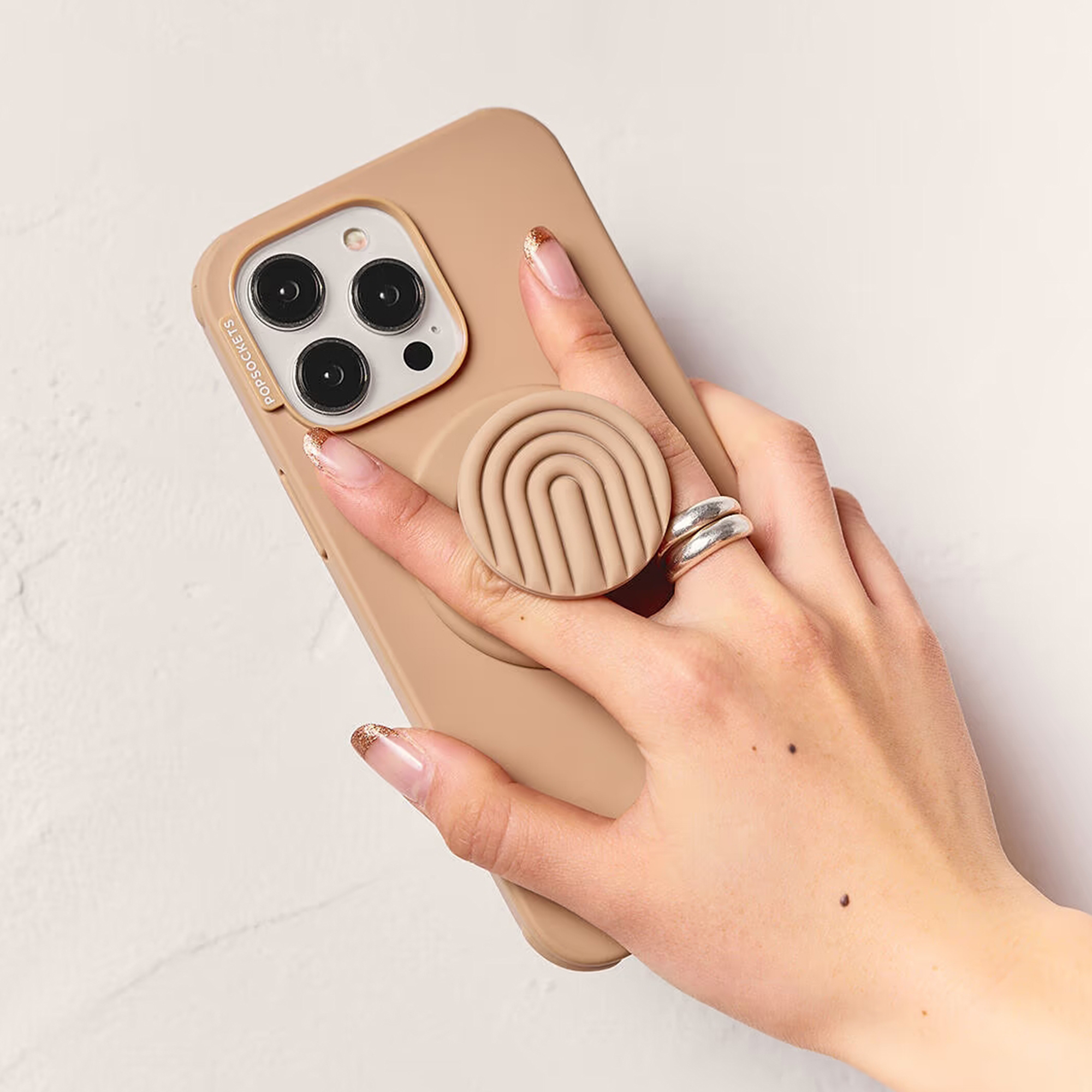 Eine Hand mit Glitzernägeln hält ein beige Smartphone mit PopGrip.