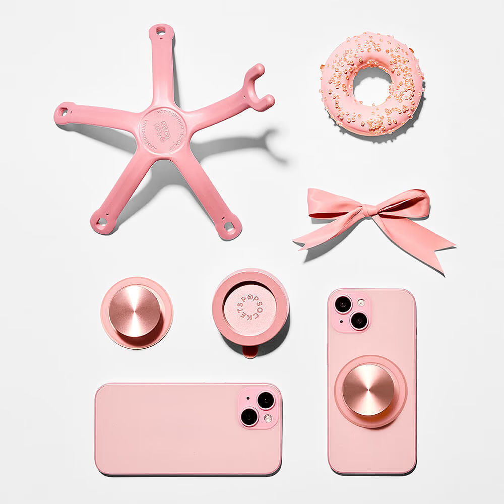 Eine Anordnung rosa Gegenstände auf Weiß, darunter zwei Handys, ein Donut, eine Schleife, Handygriffe und ein Stern.