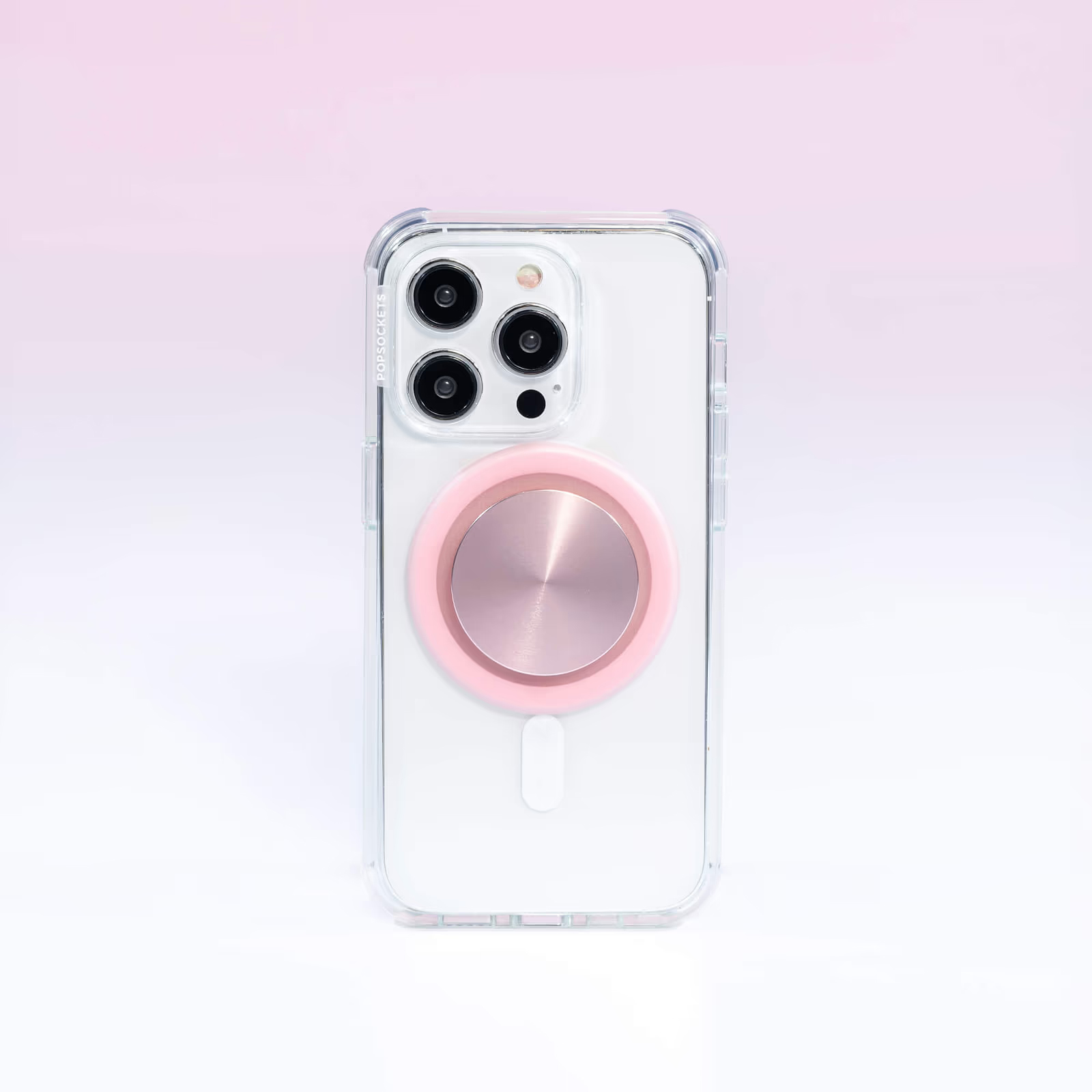 Ein weißes Smartphone in einer transparenten Hülle mit einem runden, rosa Halter auf der Rückseite vor rosa Hintergrund.