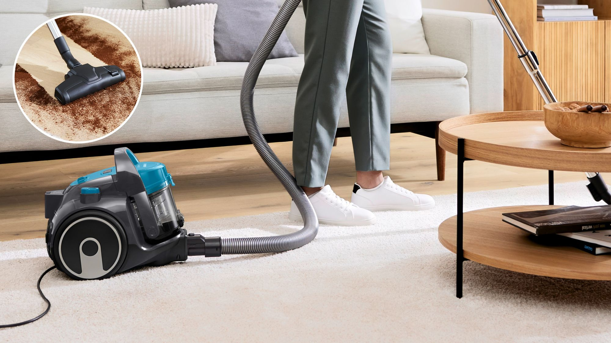 Une personne passe l'aspirateur sur un tapis clair avec un aspirateur gris foncé et bleu.