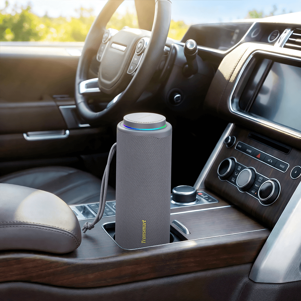 Ein grauer zylindrischer Bluetooth-Lautsprecher steht im Getränkehalter einer luxuriösen Auto-Mittelkonsole.