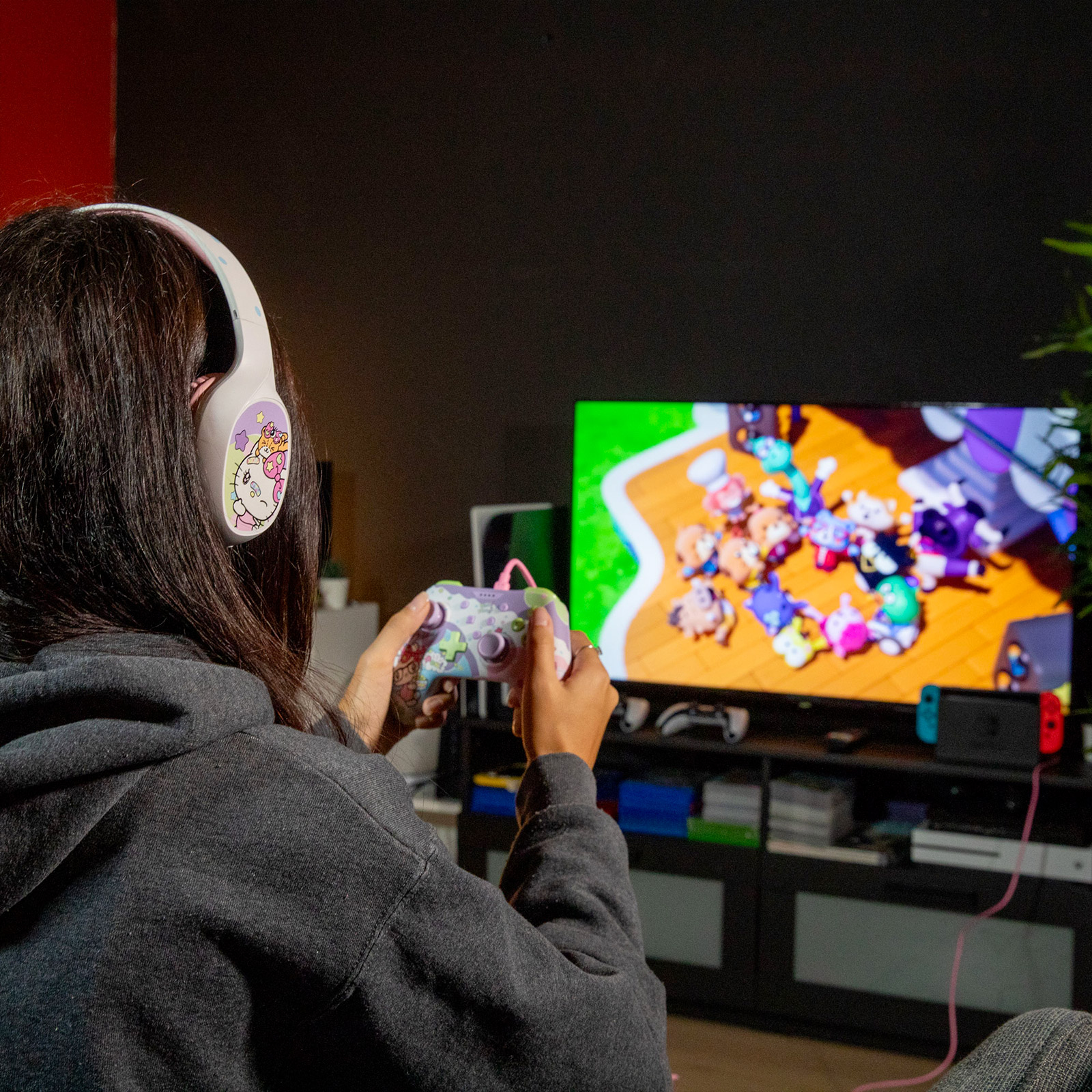 Person mit weißem Headset hält bunten Controller und spielt Videospiele vor dem Fernseher.