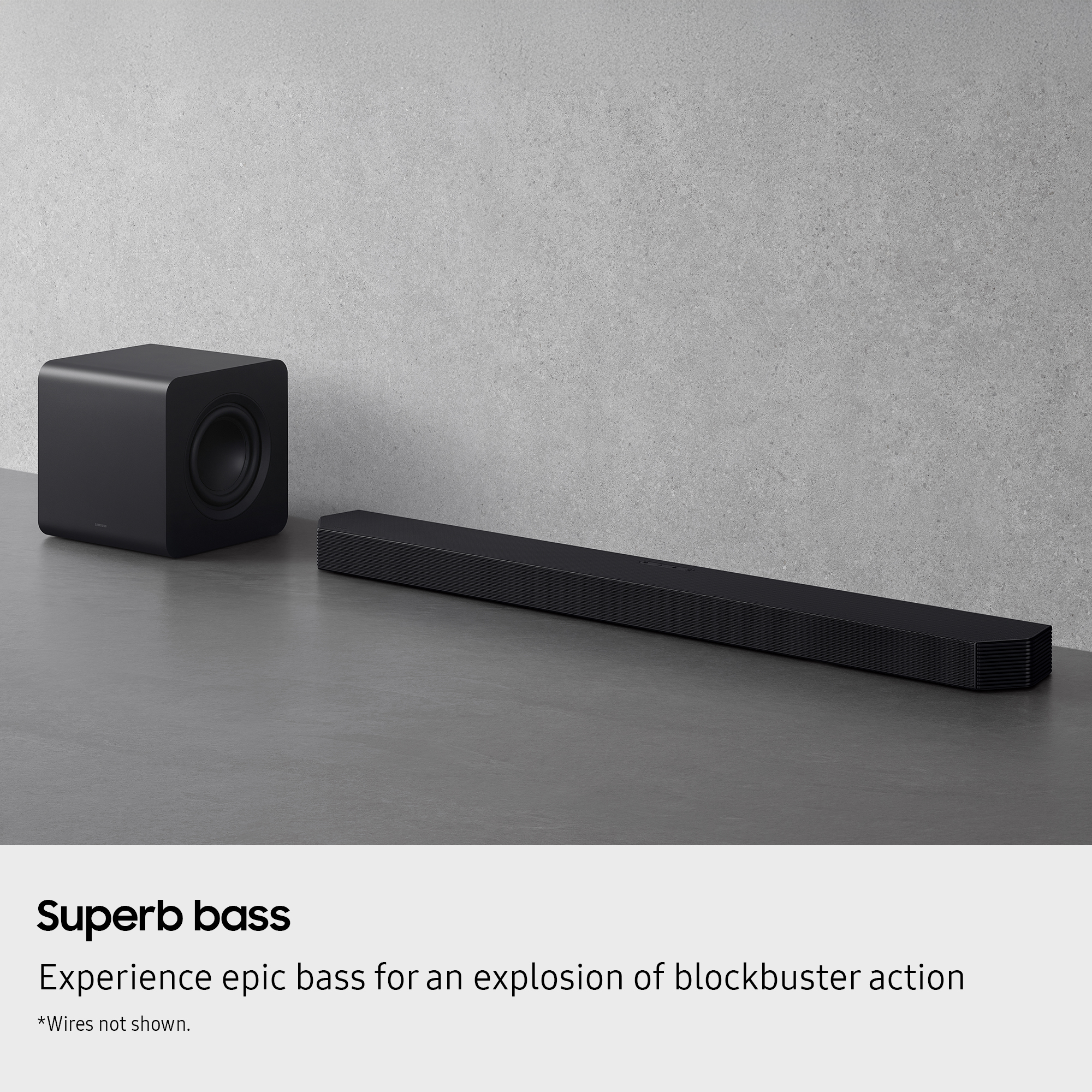 Un subwoofer nero e una soundbar su una superficie grigia contro una parete grigio chiaro.