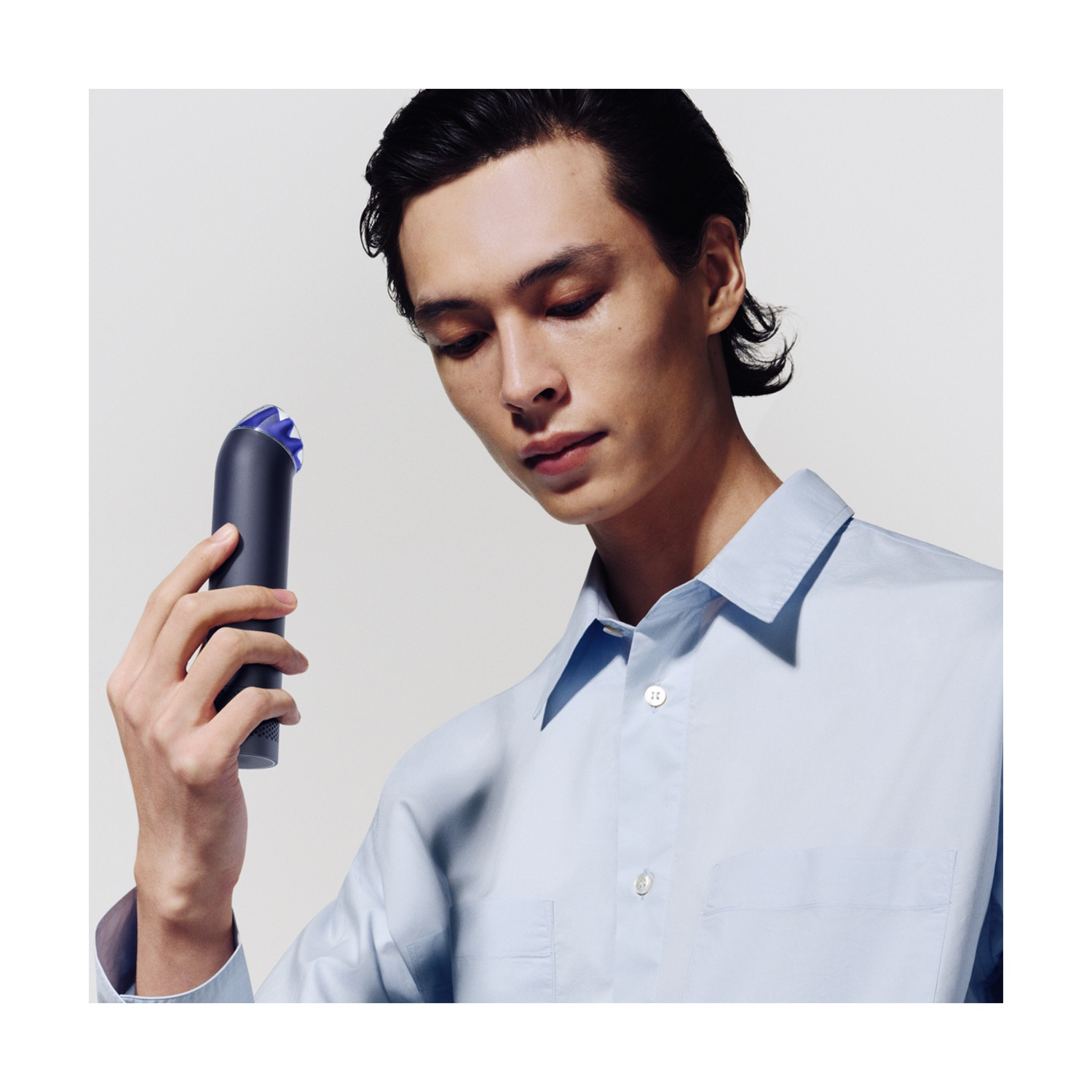 Ein Mann in einem hellblauen Hemd hält ein dunkelgraues Styling-Tool vor weißem Hintergrund.