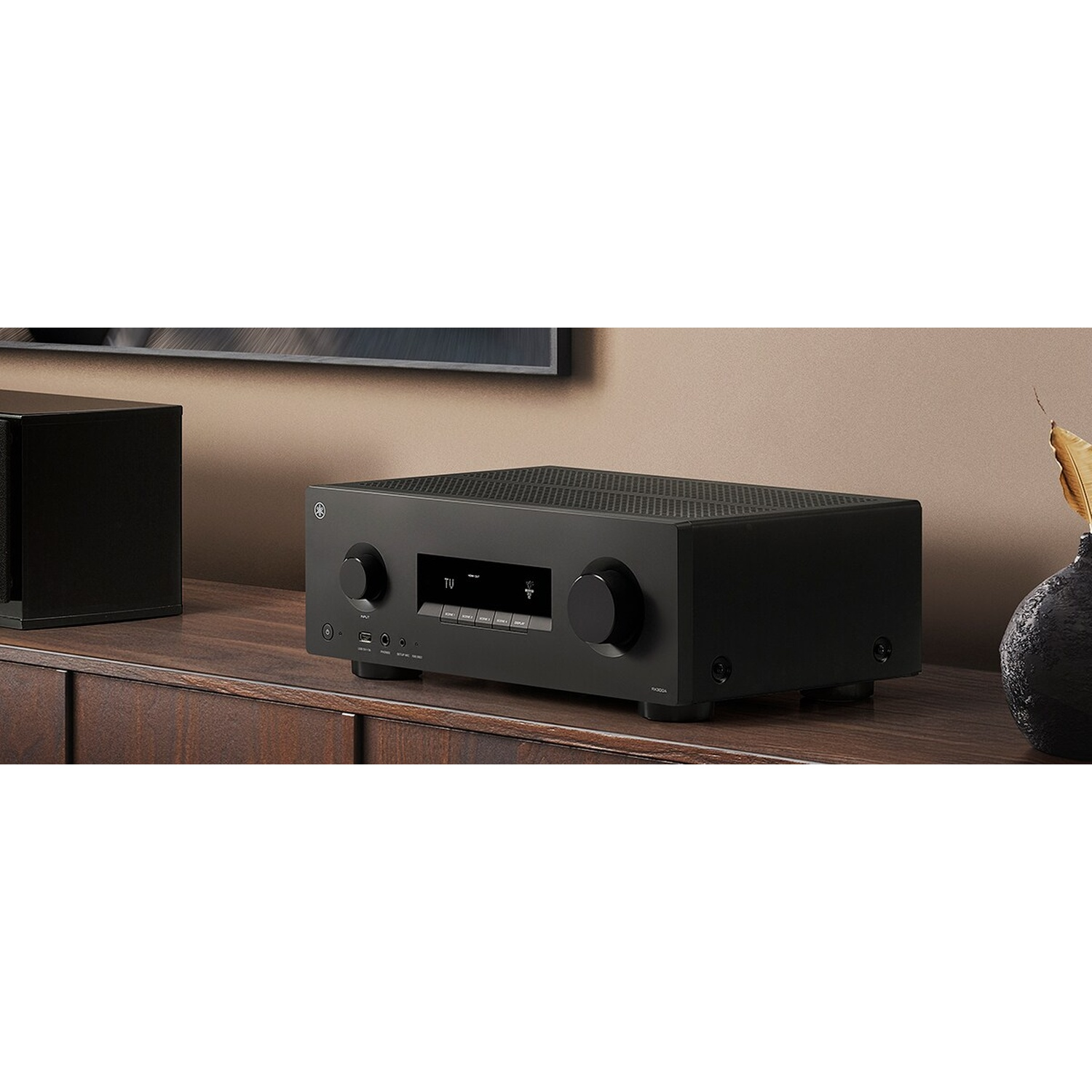 Ein schwarzer AV-Receiver steht auf einem Holzschrank in einem Raum.