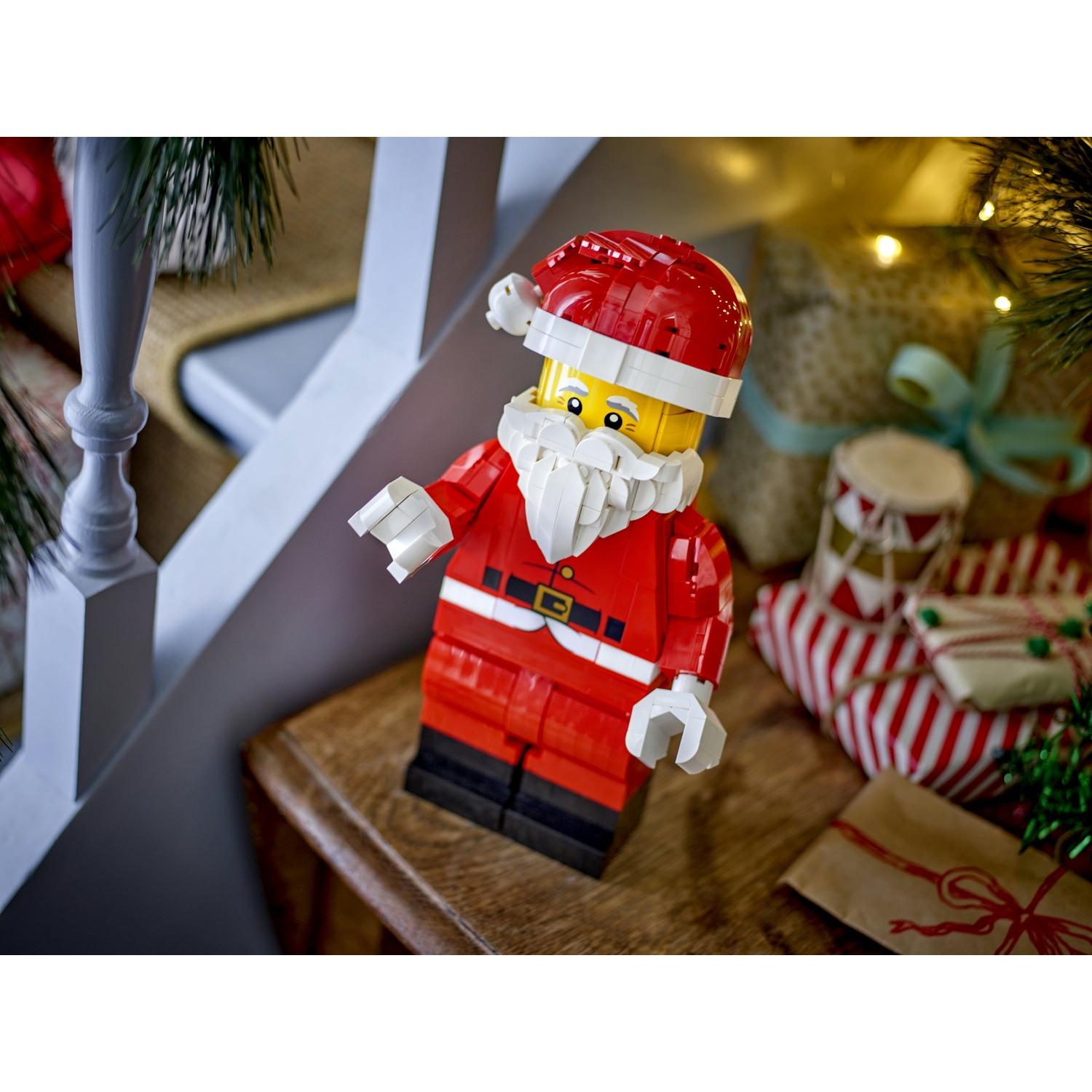 Figurka Świętego Mikołaja z Lego stoi na drewnianym stole obok zapakowanych prezentów.