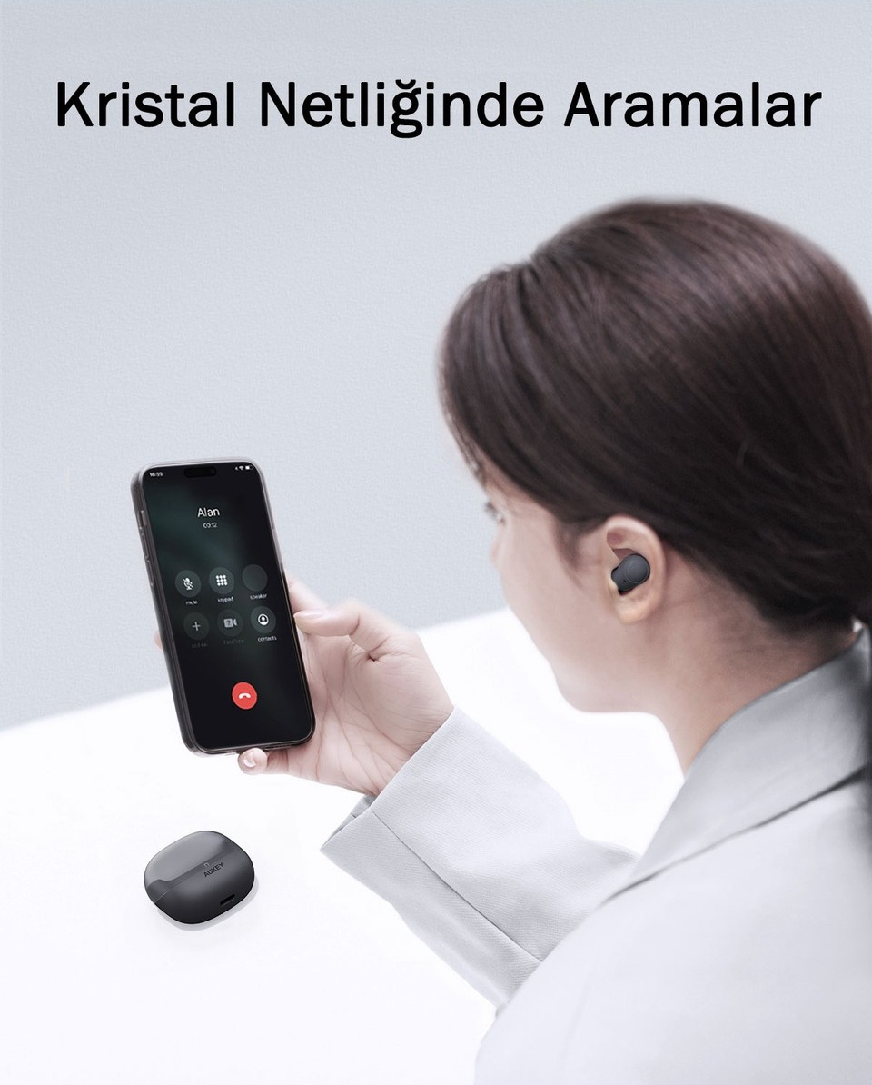 Kulaklık takan bir kadın, aktif bir çağrı ekranı olan akıllı telefonu tutuyor, masada şarj kutusu var.