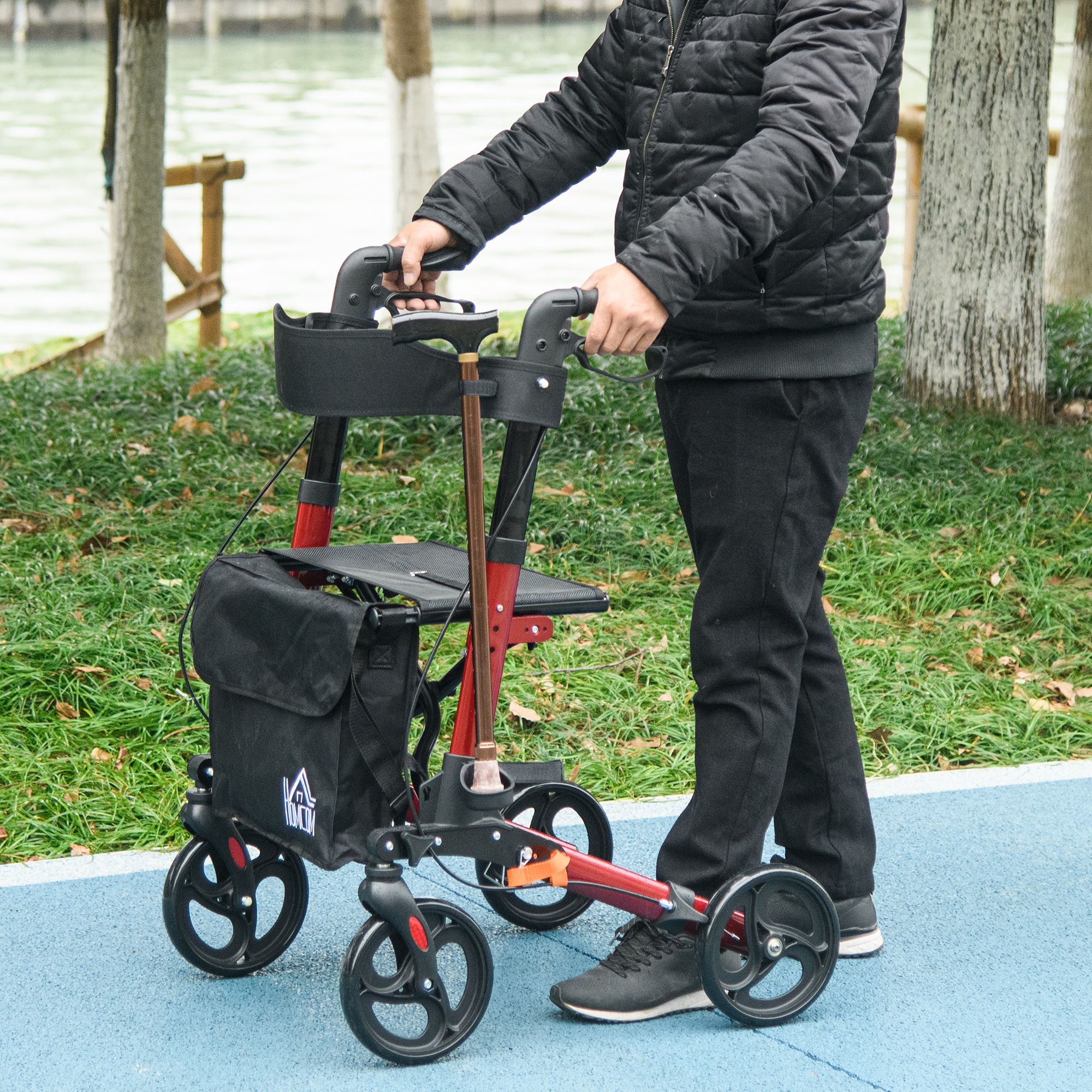 Una persona usa un andador rojo con bolsa en un sendero azul del parque.