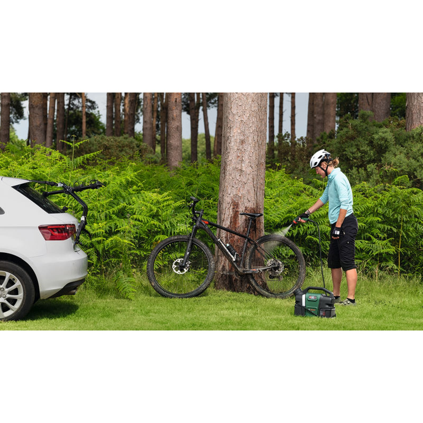 Eine Radfahrerin wäscht in einem Wald mit einem mobilen Hochdruckreiniger ein Mountainbike.