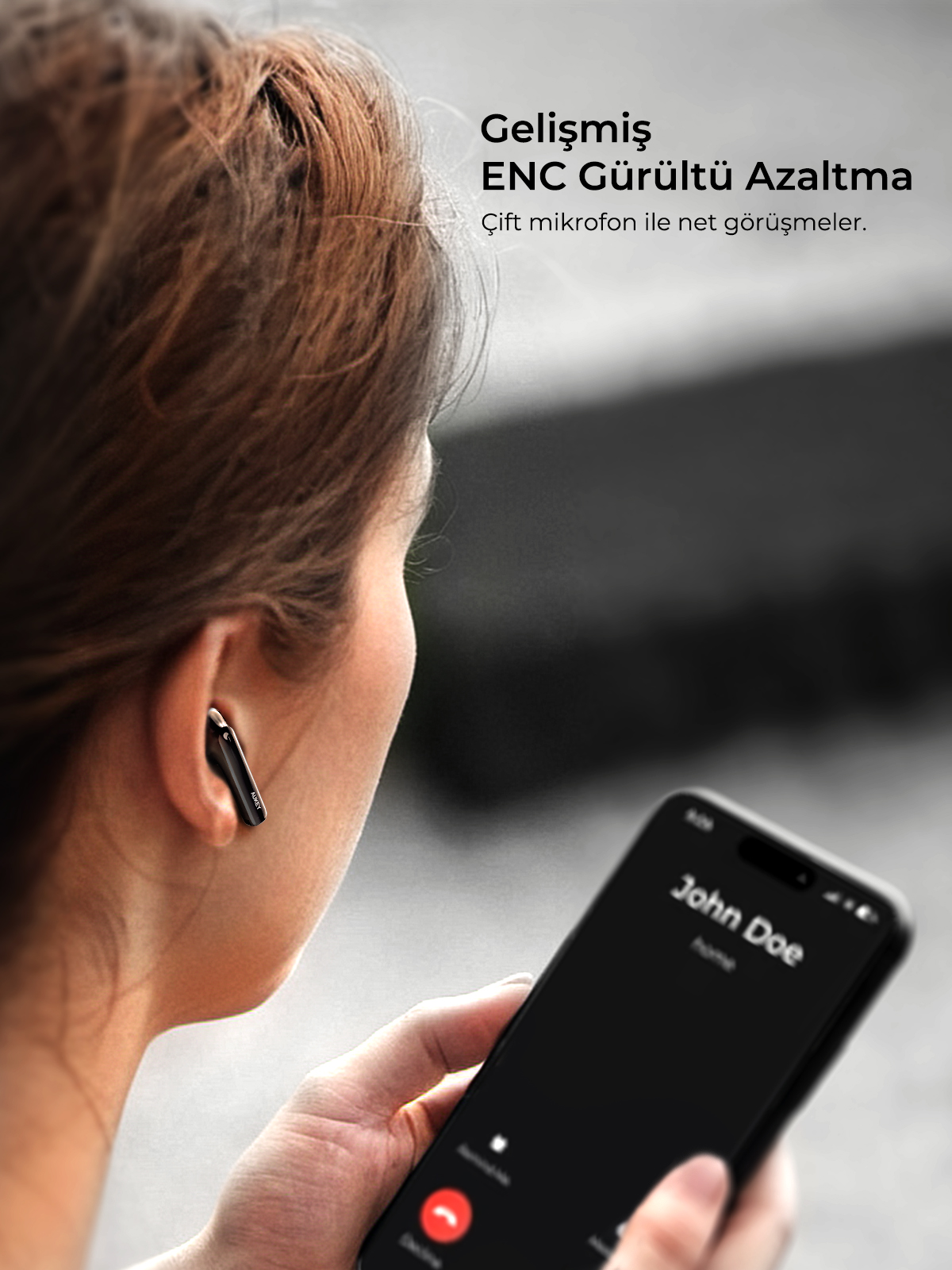 Siyah kablosuz kulaklık takan bir kadın akıllı telefonuyla arama yapıyor.