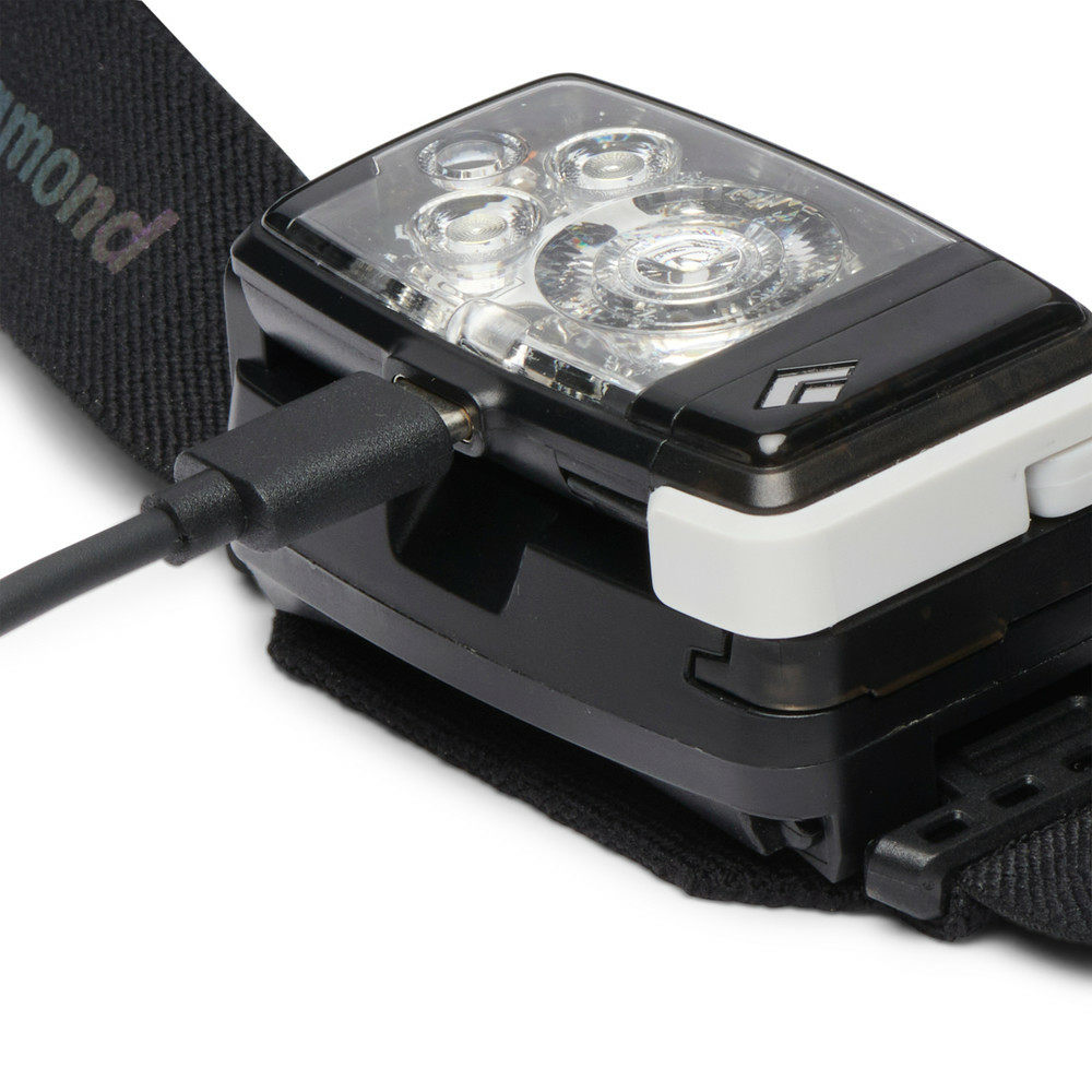 Eine schwarze Stirnlampe mit eingestecktem USB-Kabel auf einem schwarzen Gummiband vor weißem Hintergrund.