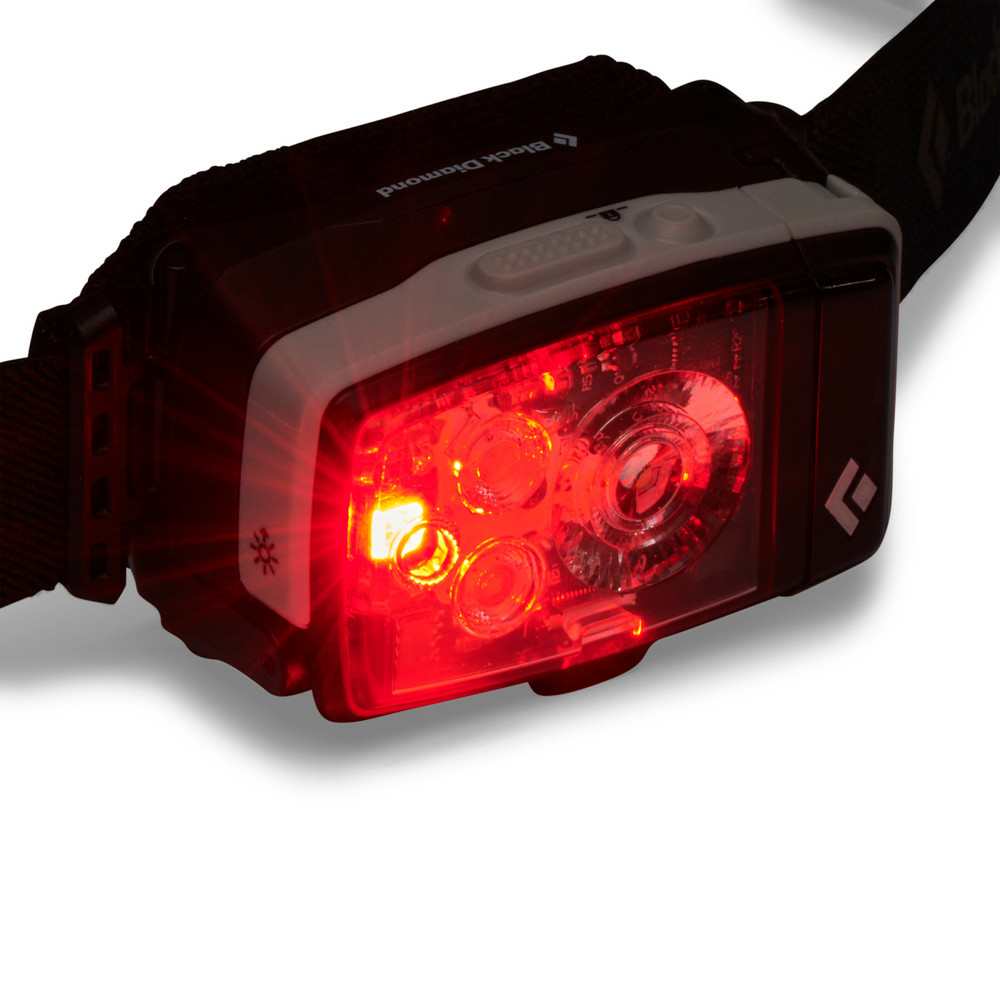 Eine schwarz-weiße Black Diamond Stirnlampe mit hellrotem LED-Licht auf der Vorderseite vor weißem Hintergrund.
