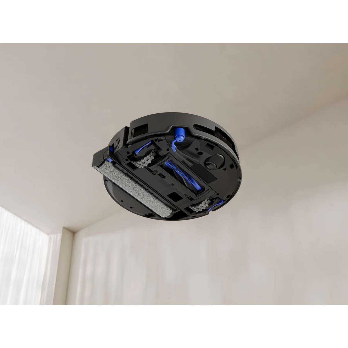 Unterseite eines schwarzen Roboterstaubsaugers mit Walzen und Rädern vor heller Zimmerwand.