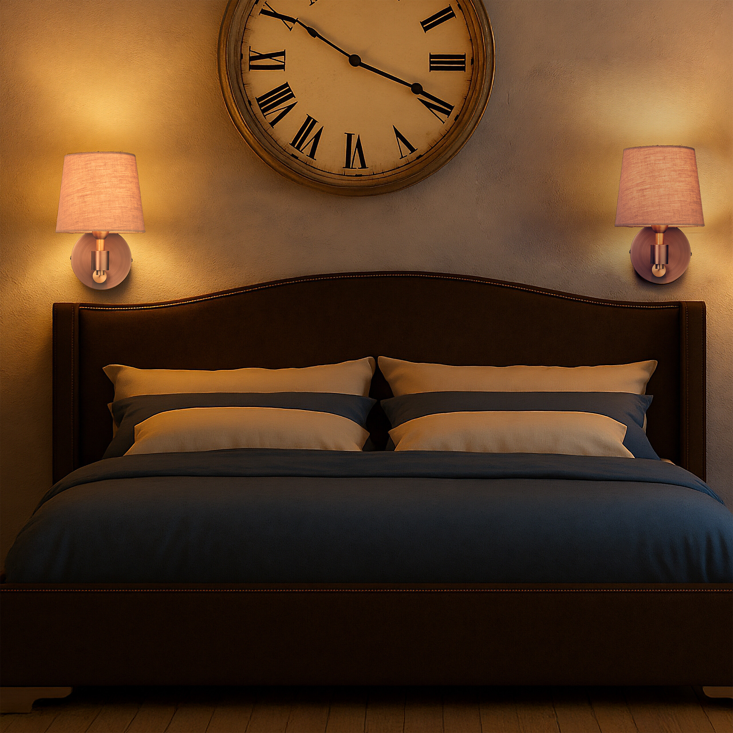 Ein Bett mit blauer Bettwäsche, Kissen, zwei Wandlampen und einer großen runden Uhr an der beige Wand.