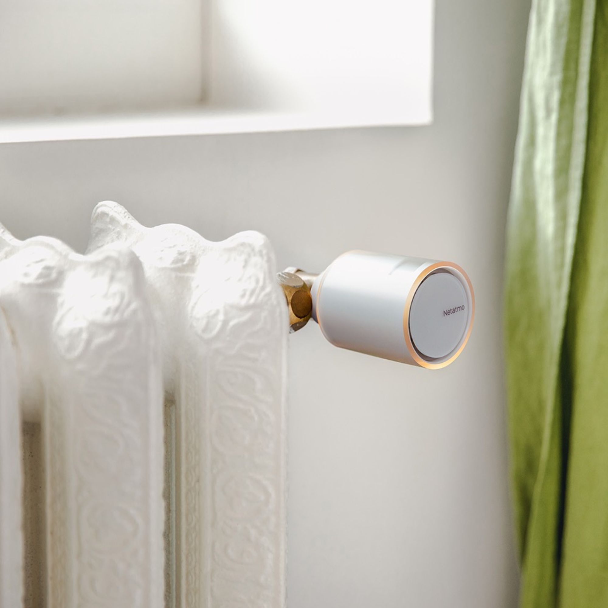 Een witte decoratieve radiator met een zilver-witte slimme Netatmo radiatorthermostaat in een kamer.