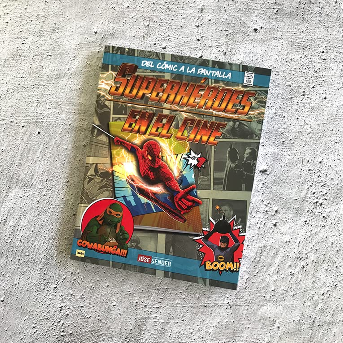 Un libro titulado "Superhéroes en el Cine" sobre una superficie de piedra gris, con varios personajes de cómics.