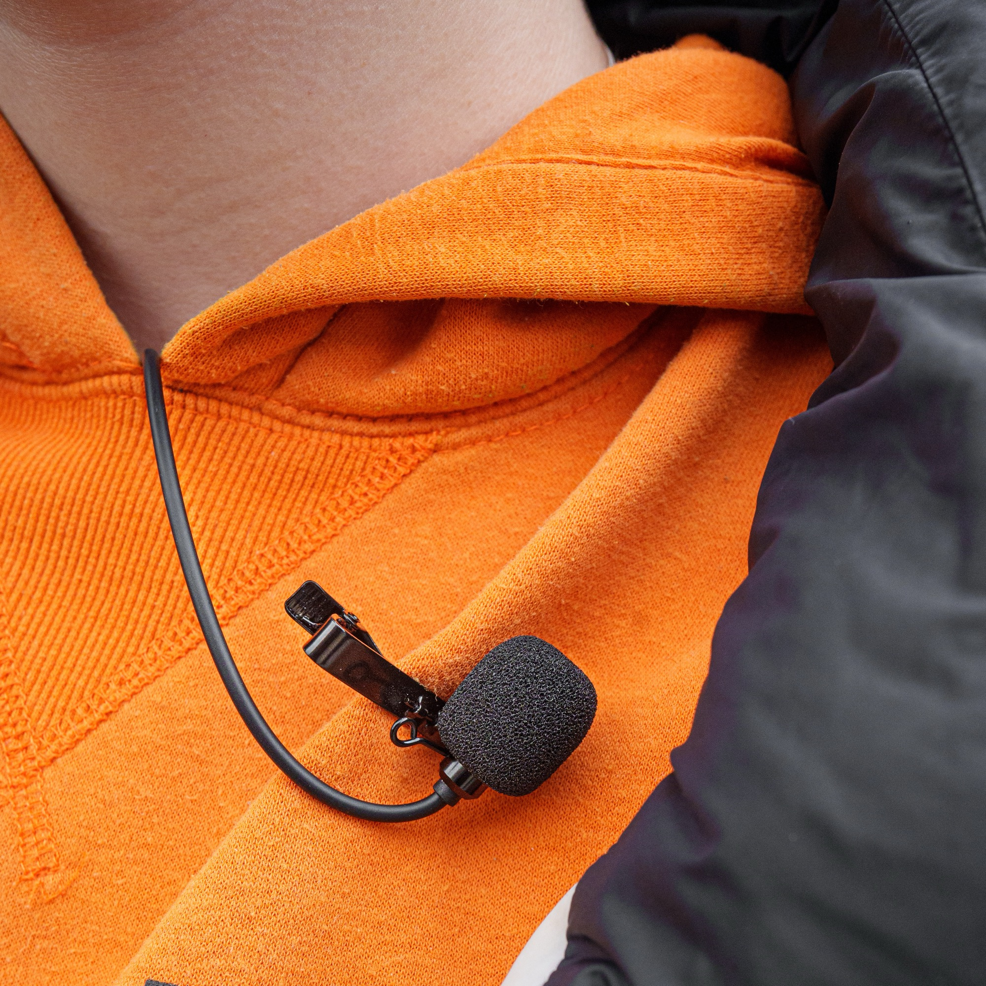 Een zwarte opspeldmicrofoon met klem is bevestigd aan een oranje hoodie.