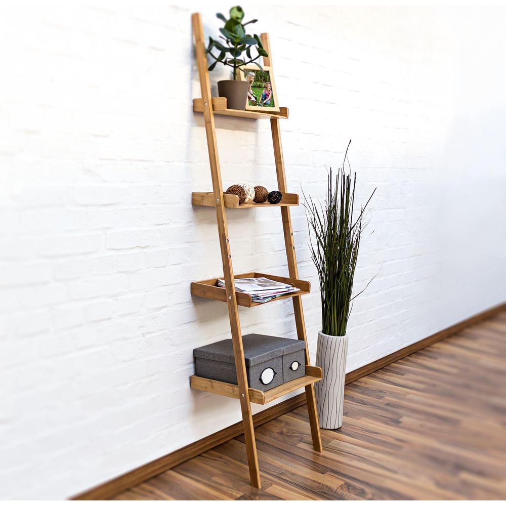 Ein hölzernes, lehnendes Regal an einer weißen Wand mit Pflanzen und Dekor. Rechts steht eine Vase mit hohen Gräsern.