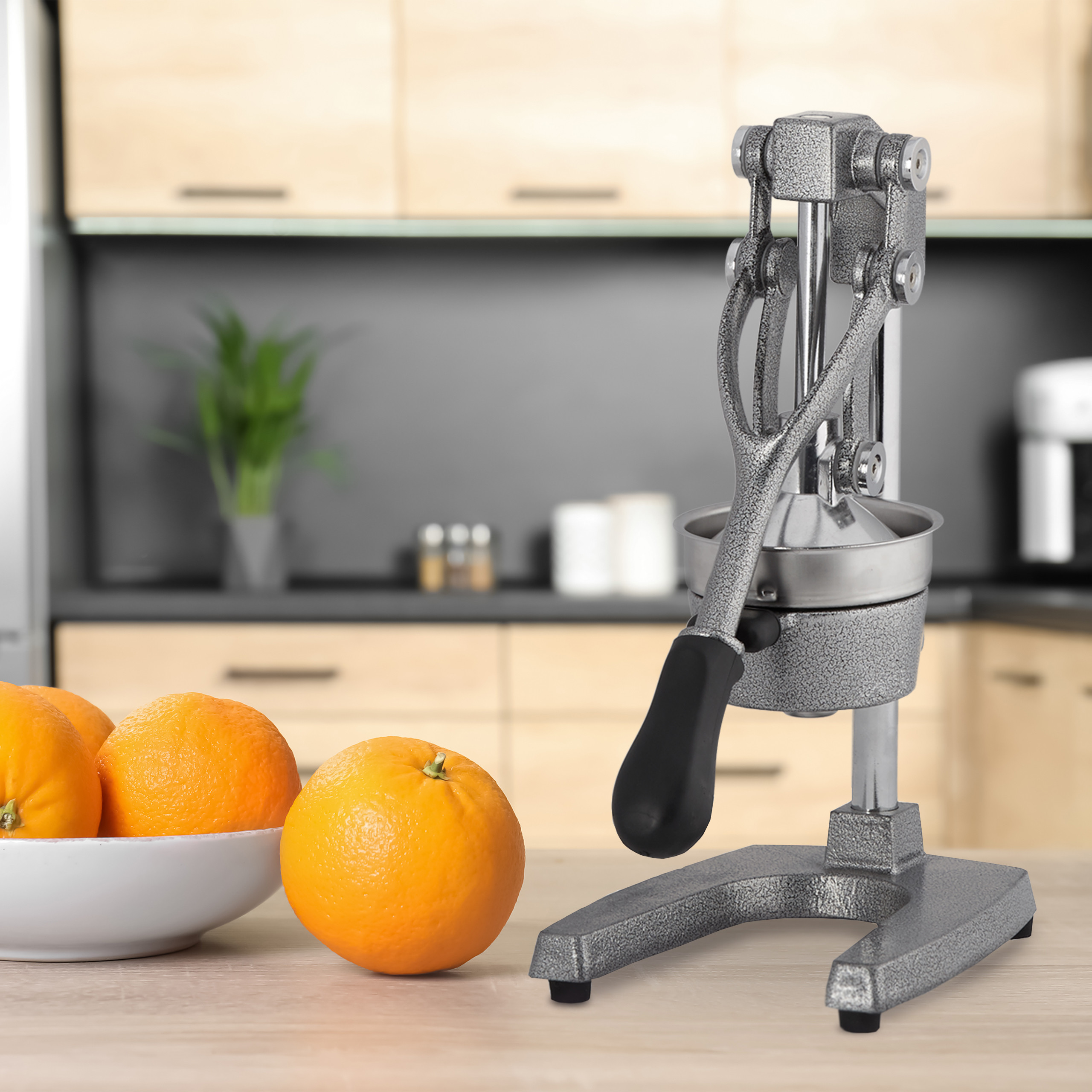 Eine Handorangenpresse aus Metall steht auf einer Holzarbeitsplatte neben einer Schüssel mit frischen Orangen.