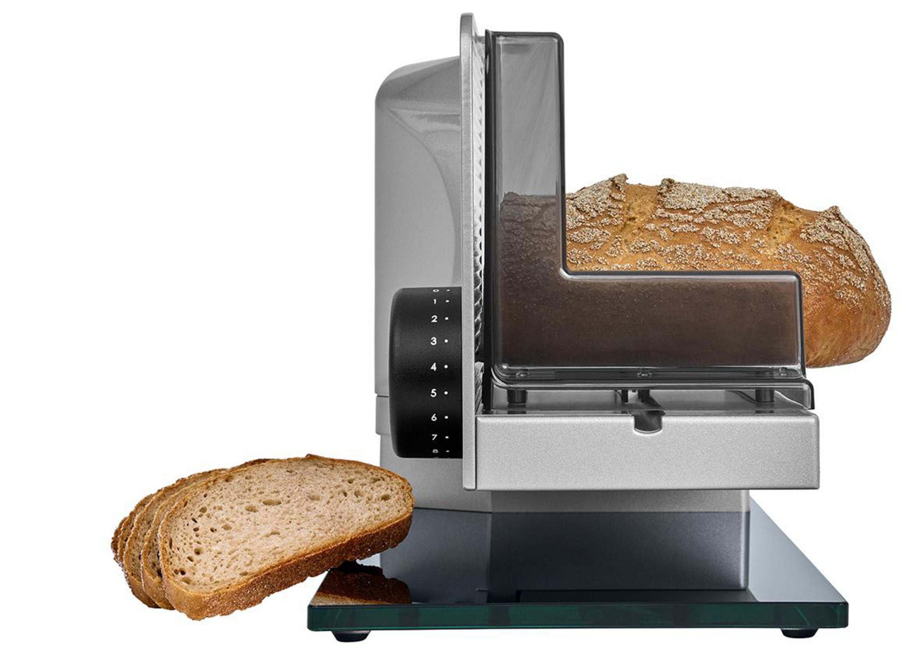 Un'affettatrice per pane argentata taglia una pagnotta, con alcune fette in primo piano.