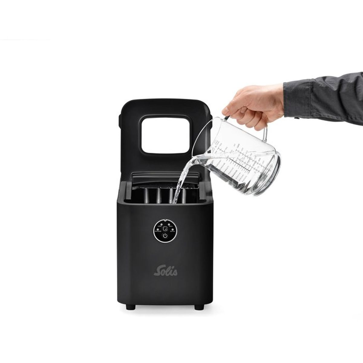 Eine Hand giesst Wasser aus einem Messbecher in einen schwarzen Solis Eisbereiter auf einem weissen Tisch.