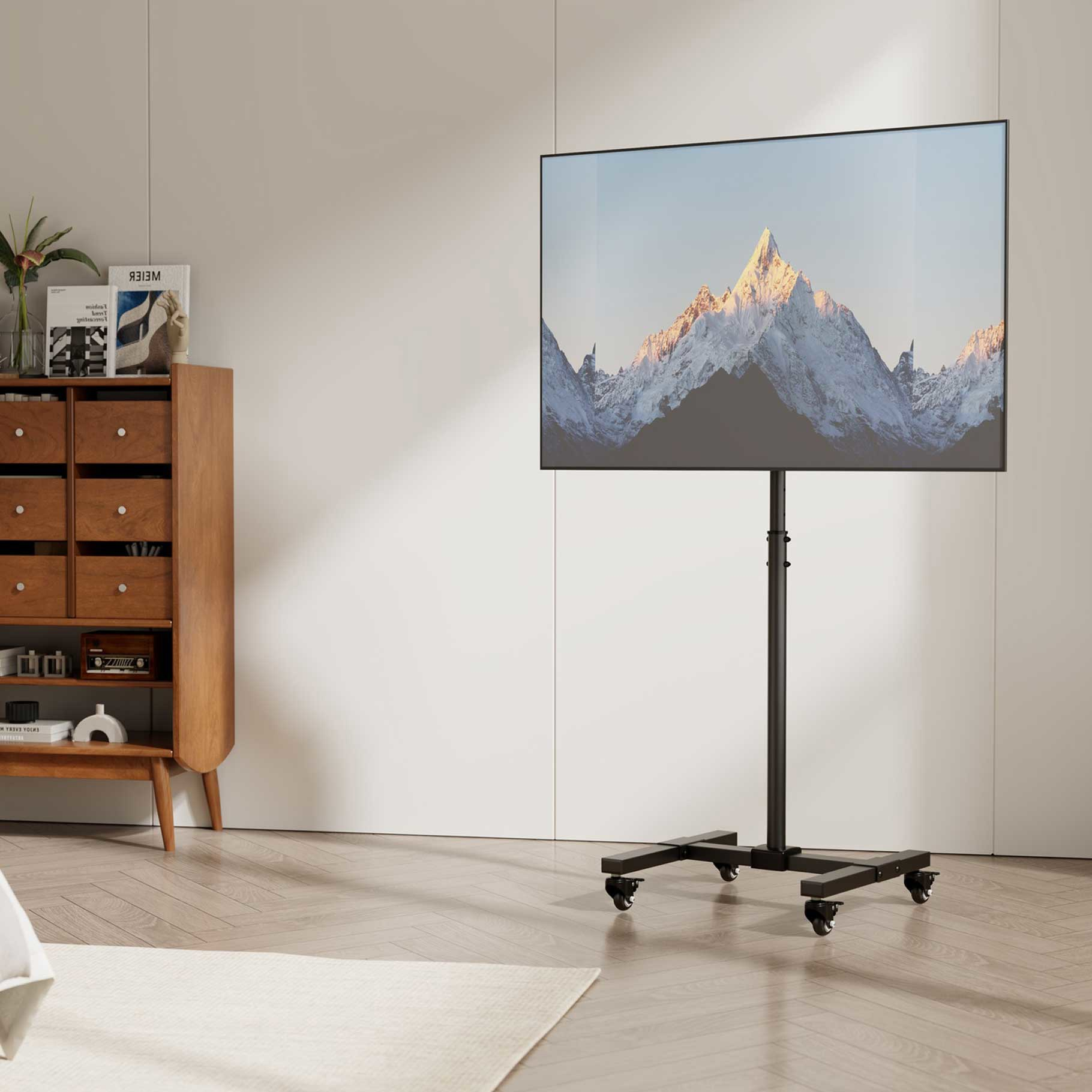 Un televisor en un soporte con ruedas muestra montañas nevadas. A la izquierda hay un mueble de madera.