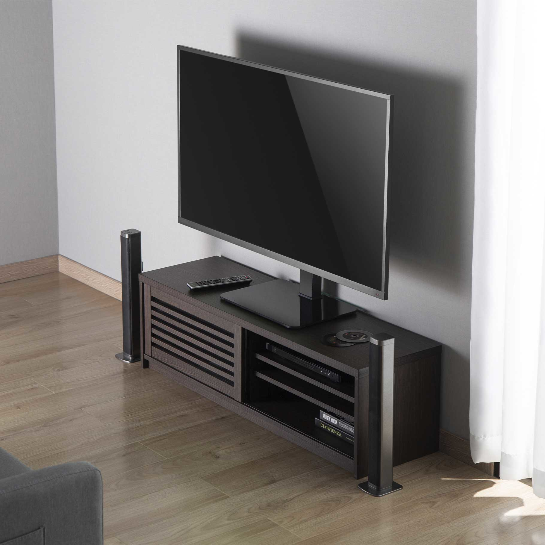 Un televisor en un mueble de madera oscura con altavoces en una habitación luminosa.