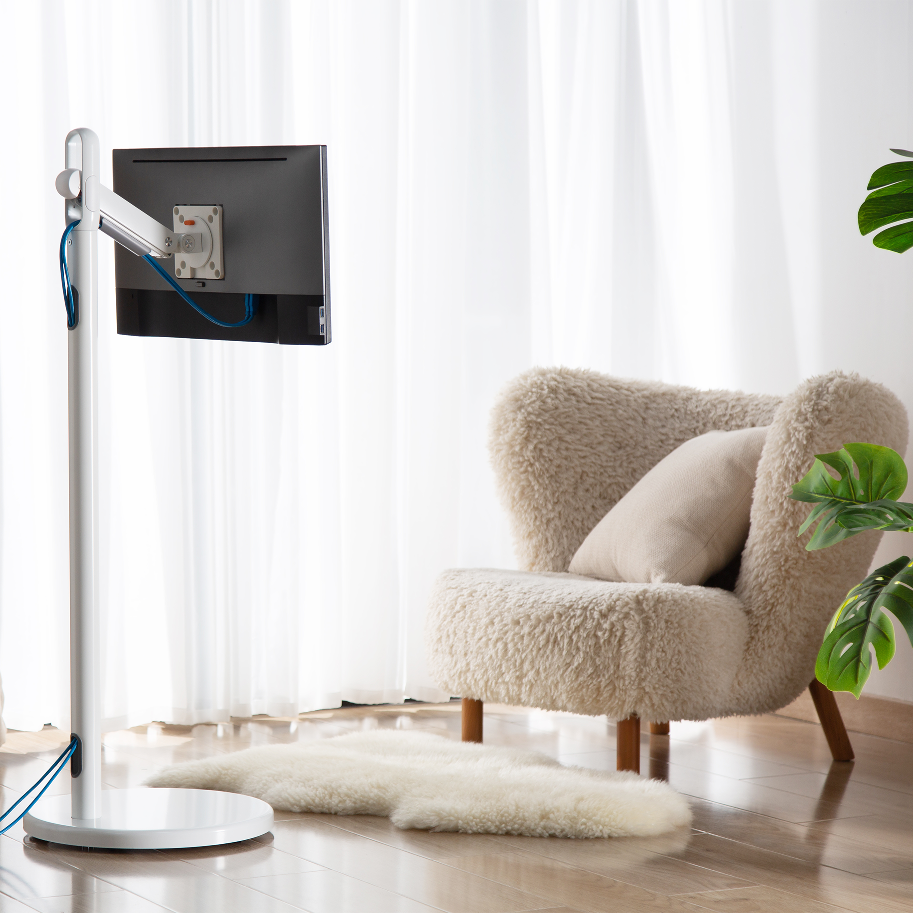 Una pantalla en un soporte blanco frente a un sillón acogedor en una habitación luminosa.