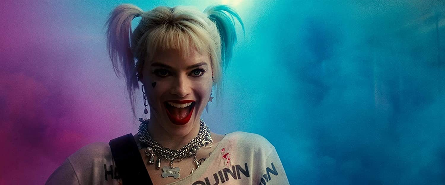Harley Quinn con coletas rubias, lápiz labial rojo y collar de plata sobre fondo rosa y azul.