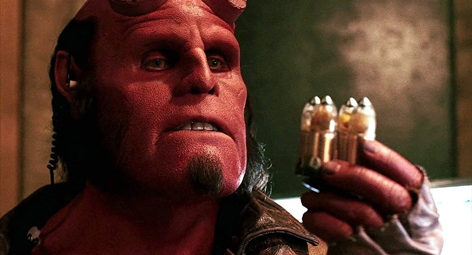 Hellboy, con piel roja, cuernos cortados y perilla, sostiene tres balas especiales en su mano.