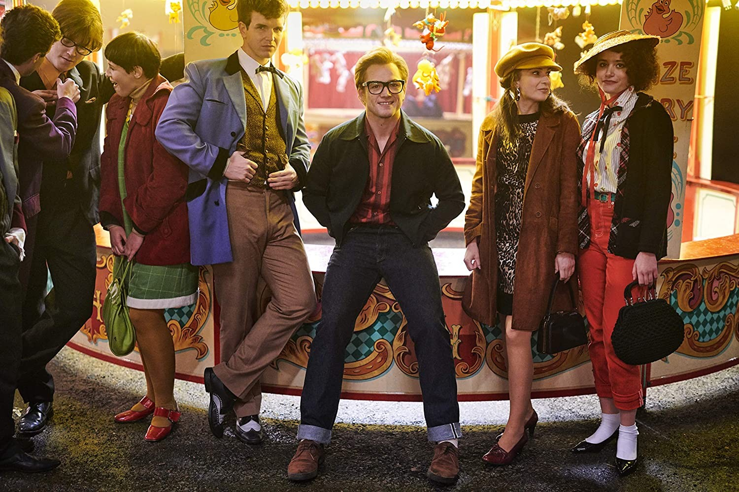 Un grupo de seis jóvenes posa frente a un colorido puesto de feria con ropa retro.