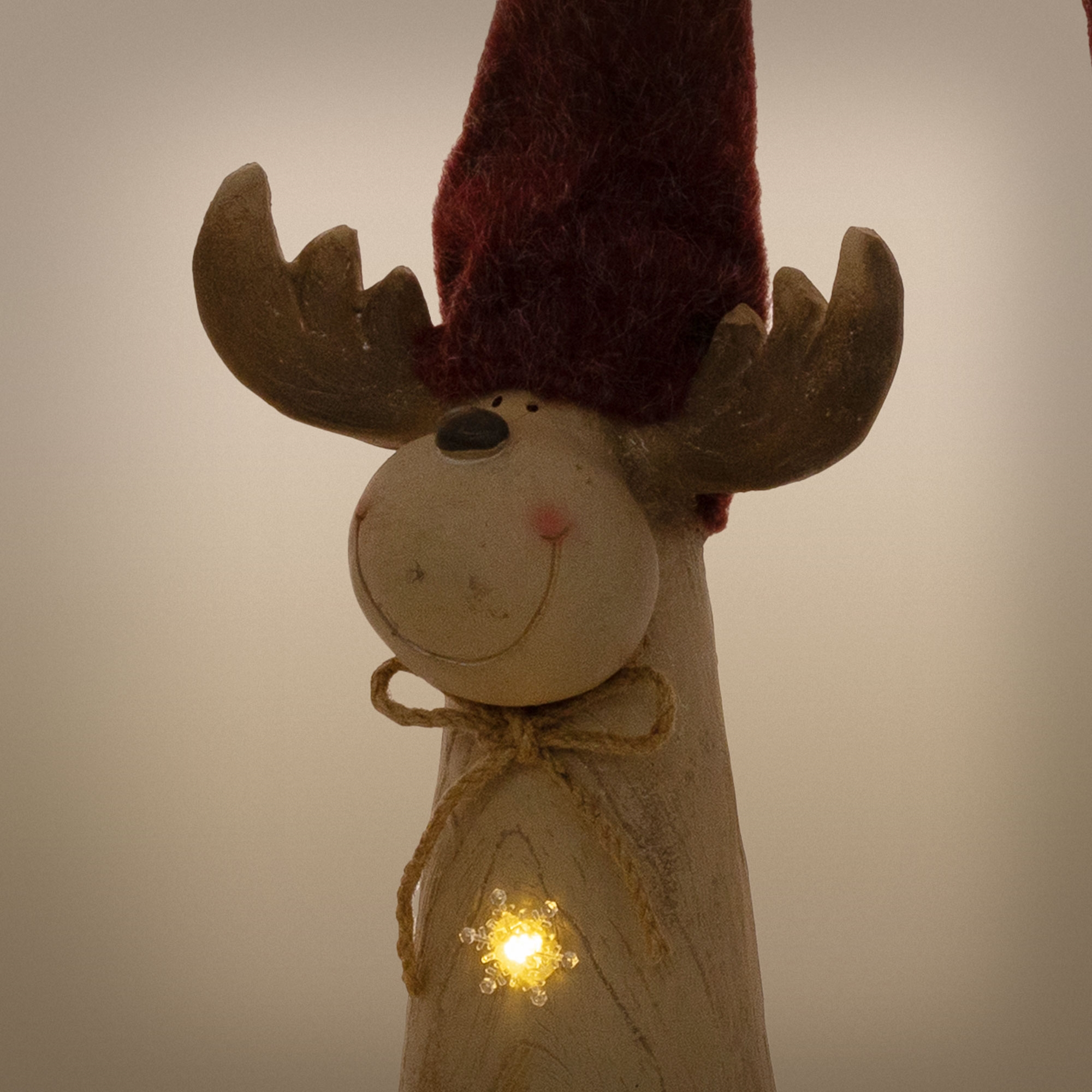 Eine hölzerne Rentierfigur mit roter Mütze, Schleife und leuchtendem Stern auf dem Körper.