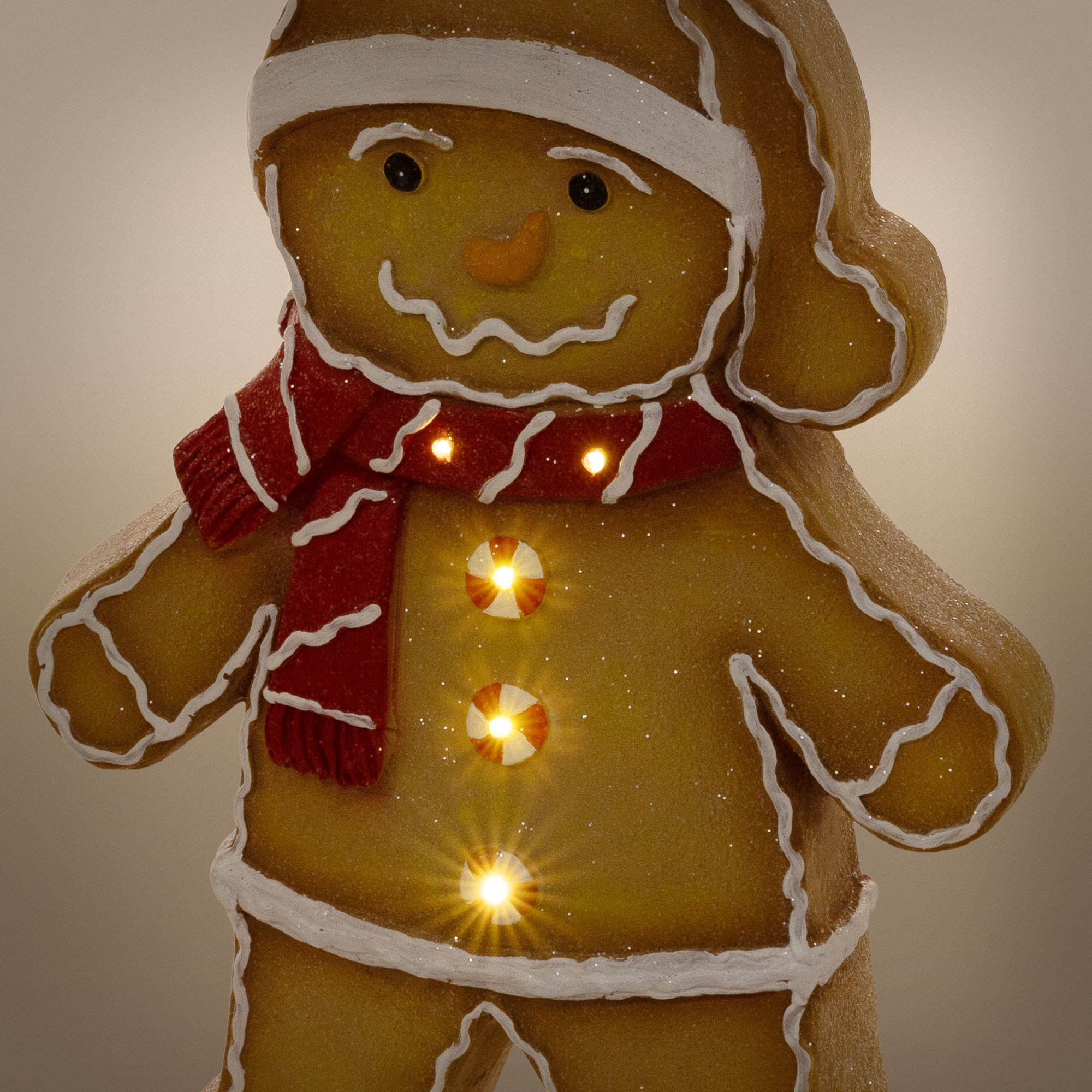 Ein beleuchteter Lebkuchenmann mit rotem Schal, Weihnachtsmütze und leuchtenden Knöpfen vor hellem Hintergrund.