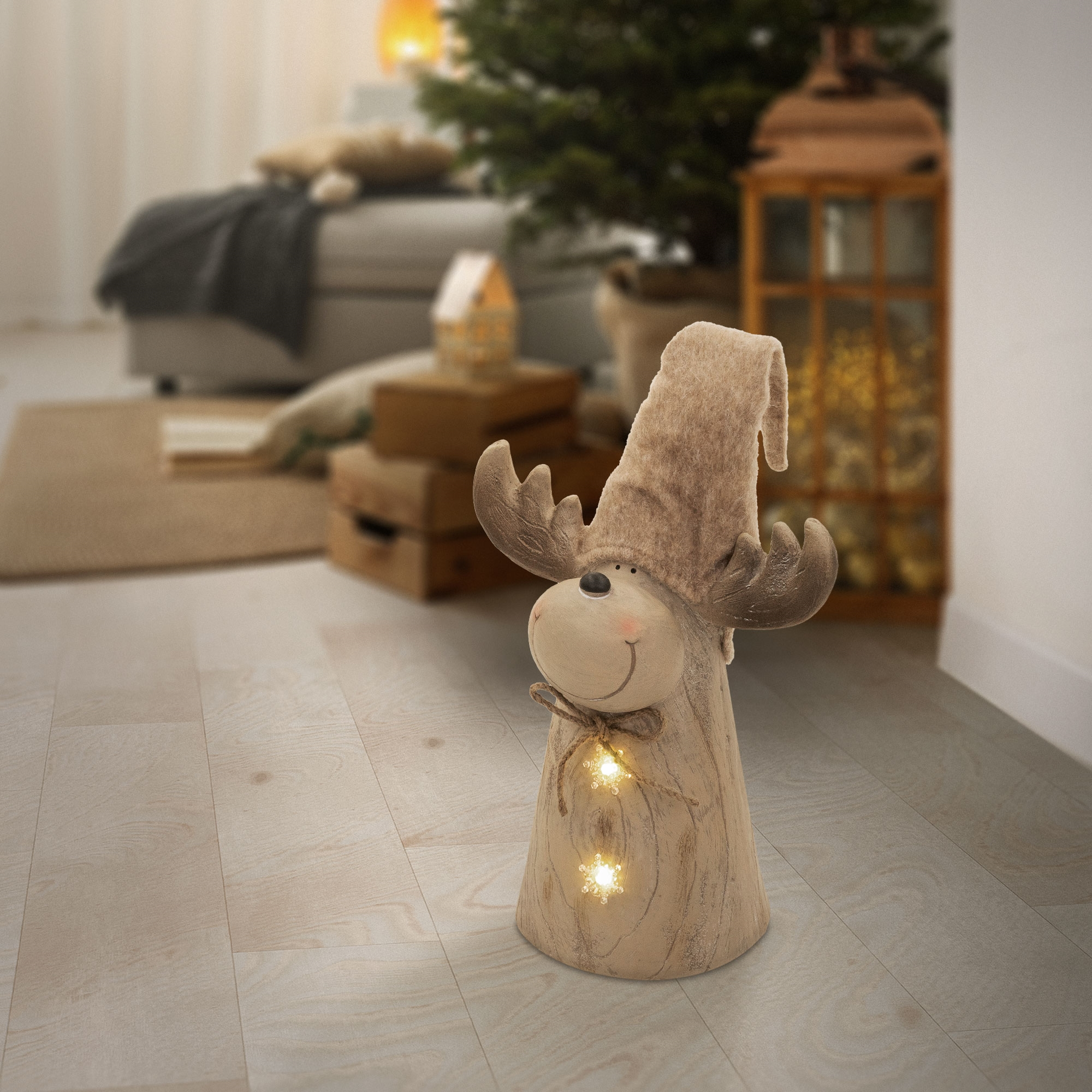 Eine hölzerne Rentierfigur mit hohem Hut und beleuchteten Sternen steht auf einem hellen Holzfußboden.