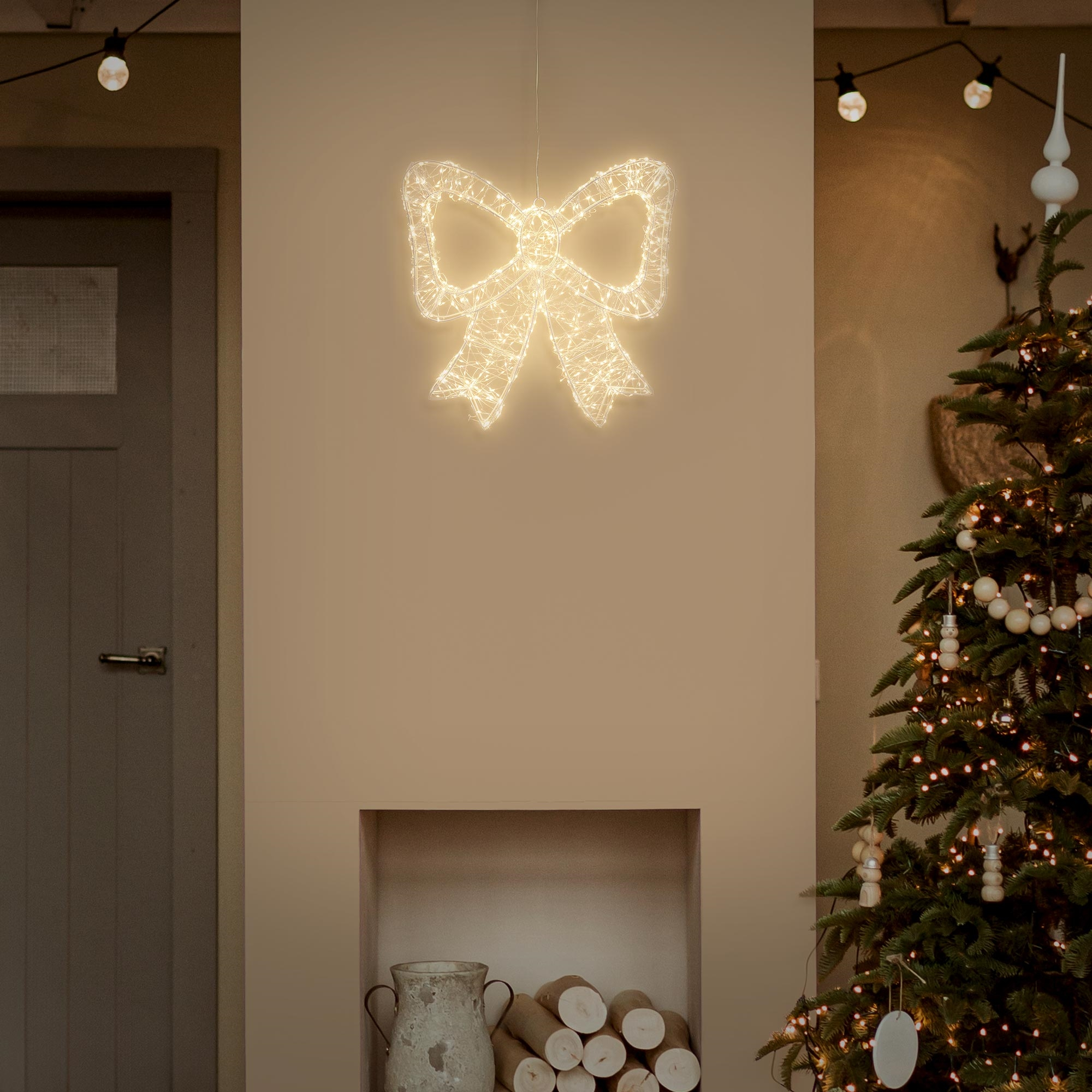 Eine leuchtende Schleife hängt an der Wand über einem Kamin neben einem Weihnachtsbaum.