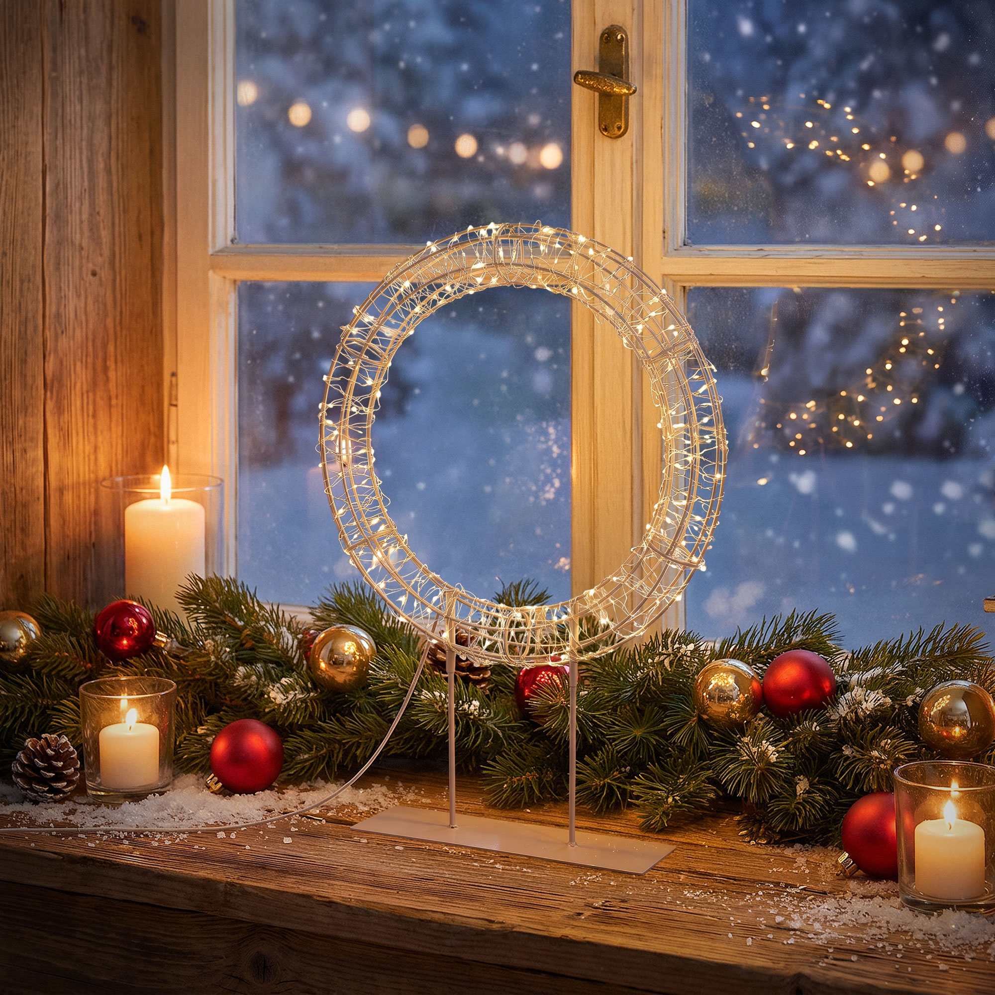 Beleuchteter Weihnachtskranz auf hölzerner Fensterbank mit Kerzen und Tannengrün.