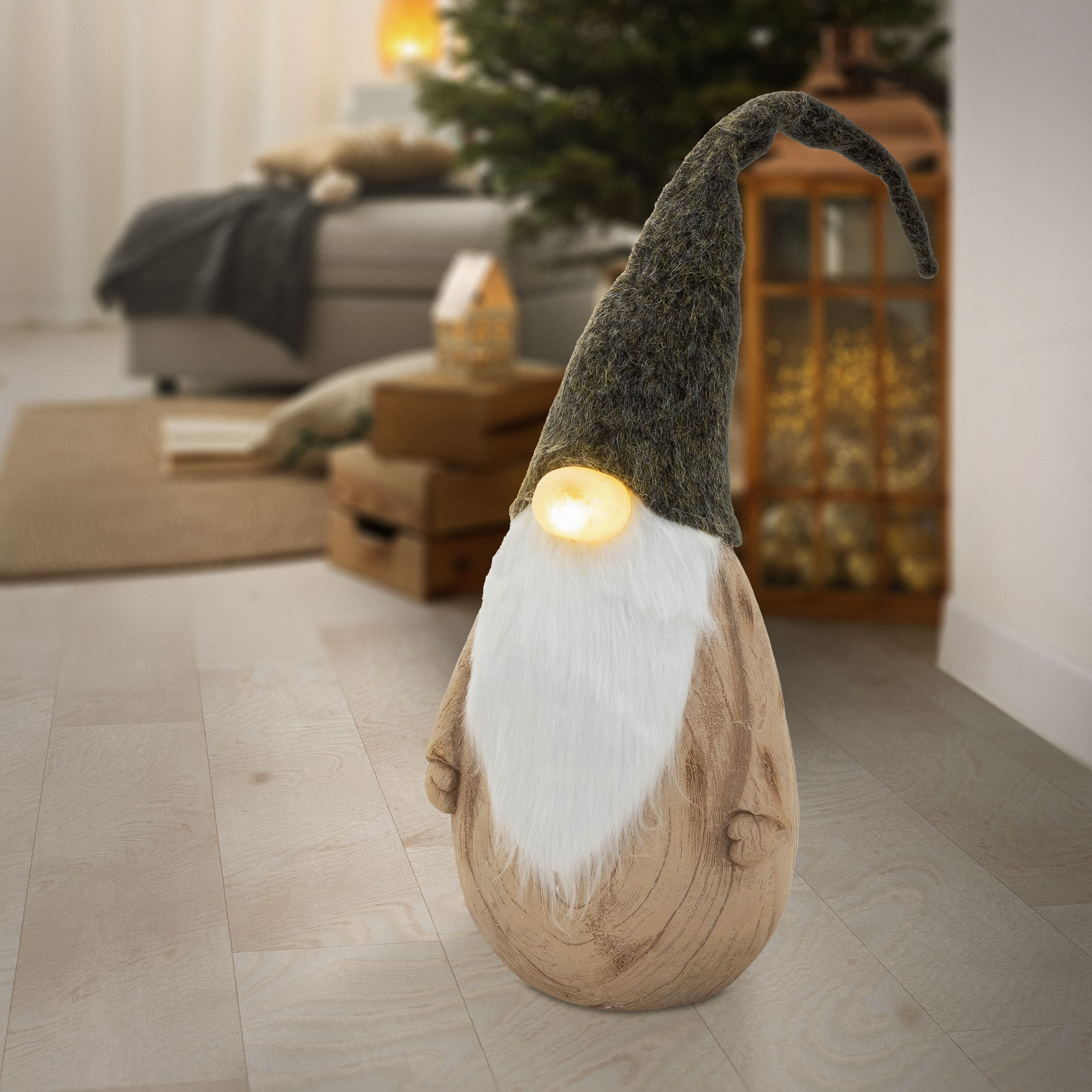 Ein hölzerner Weihnachtswichtel mit weißem Bart und langer grauer Mütze steht auf einem Holzboden in einem Zimmer.