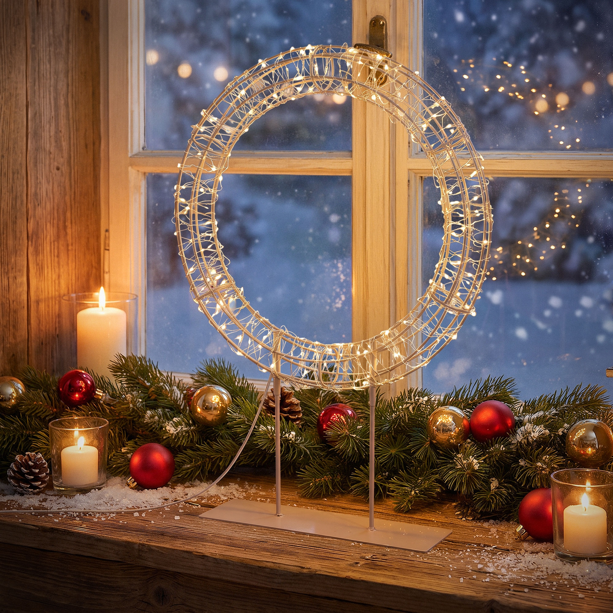Ein beleuchteter Weihnachtskranz, Kerzen und Tannengrün auf einer Holzfensterbank im Schnee.