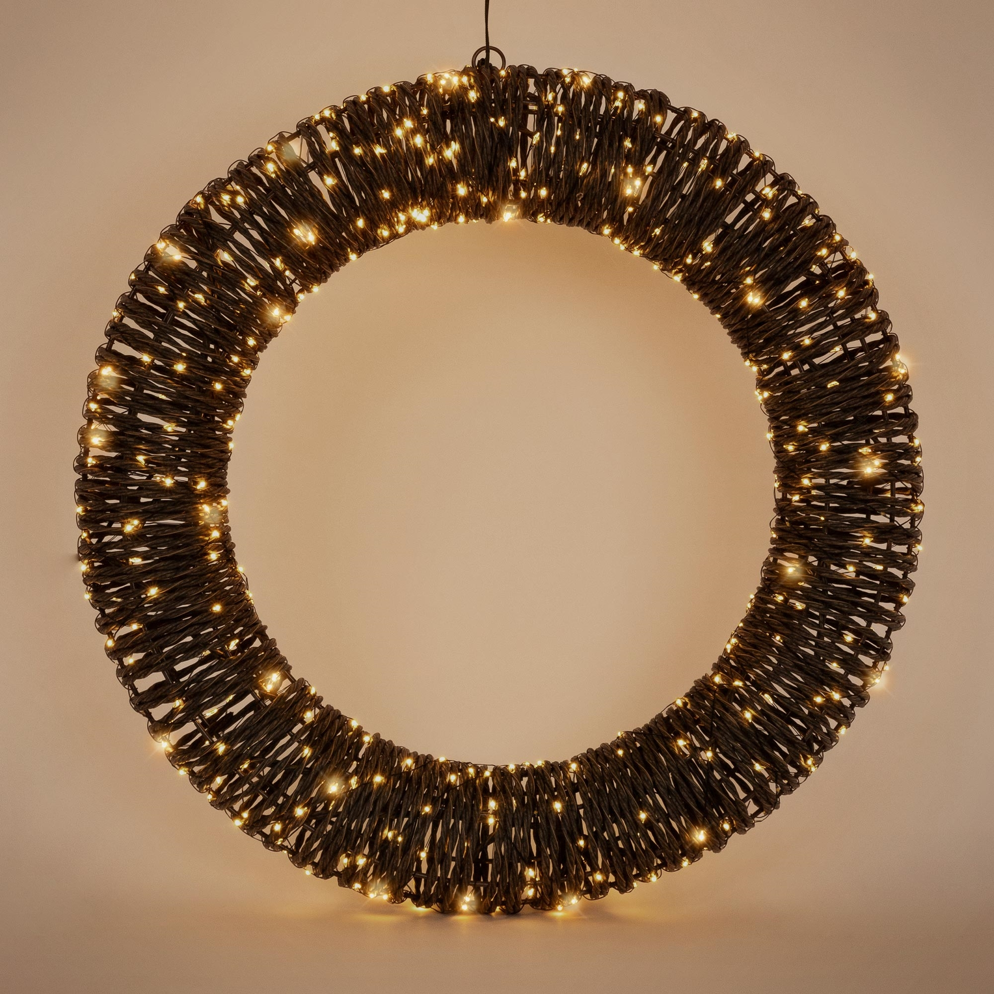 Ein beleuchteter, runder Kranz mit warmen LED-Lichtern auf beigefarbenem Hintergrund.
