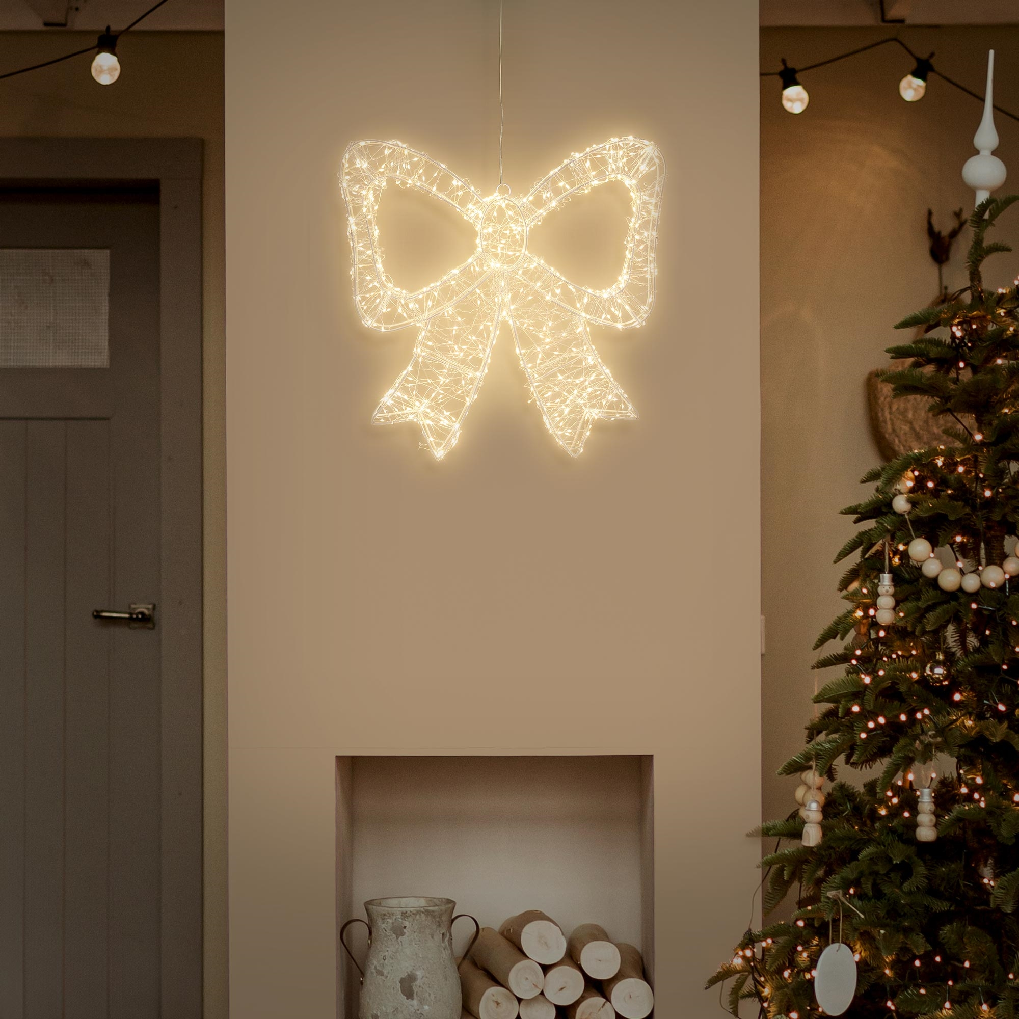 Eine leuchtende Weihnachtsmasche hängt vor einer Wand, neben einer geschmückten Tanne.