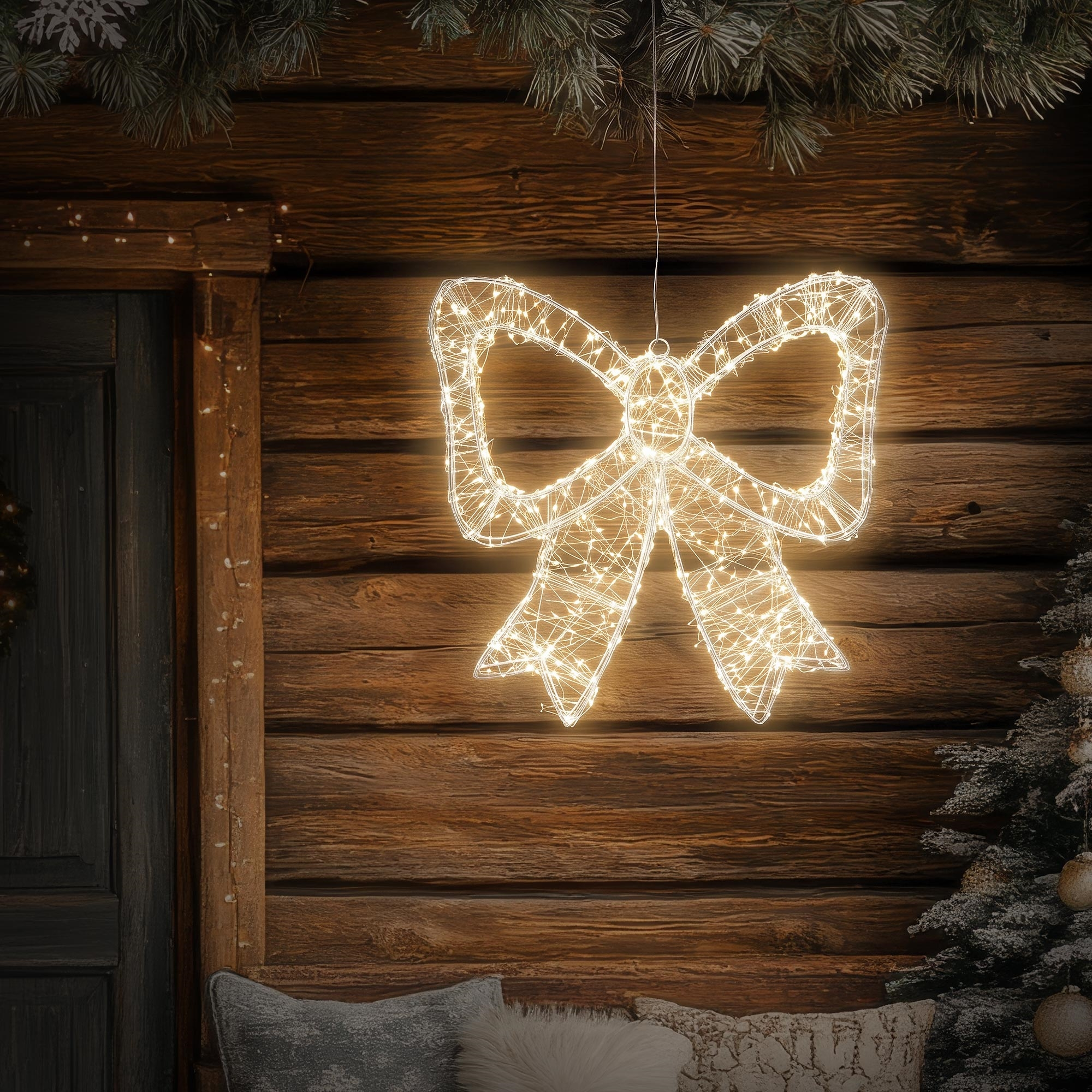 Eine leuchtende Weihnachts-Schleife hängt vor einer dunklen Holzwand.