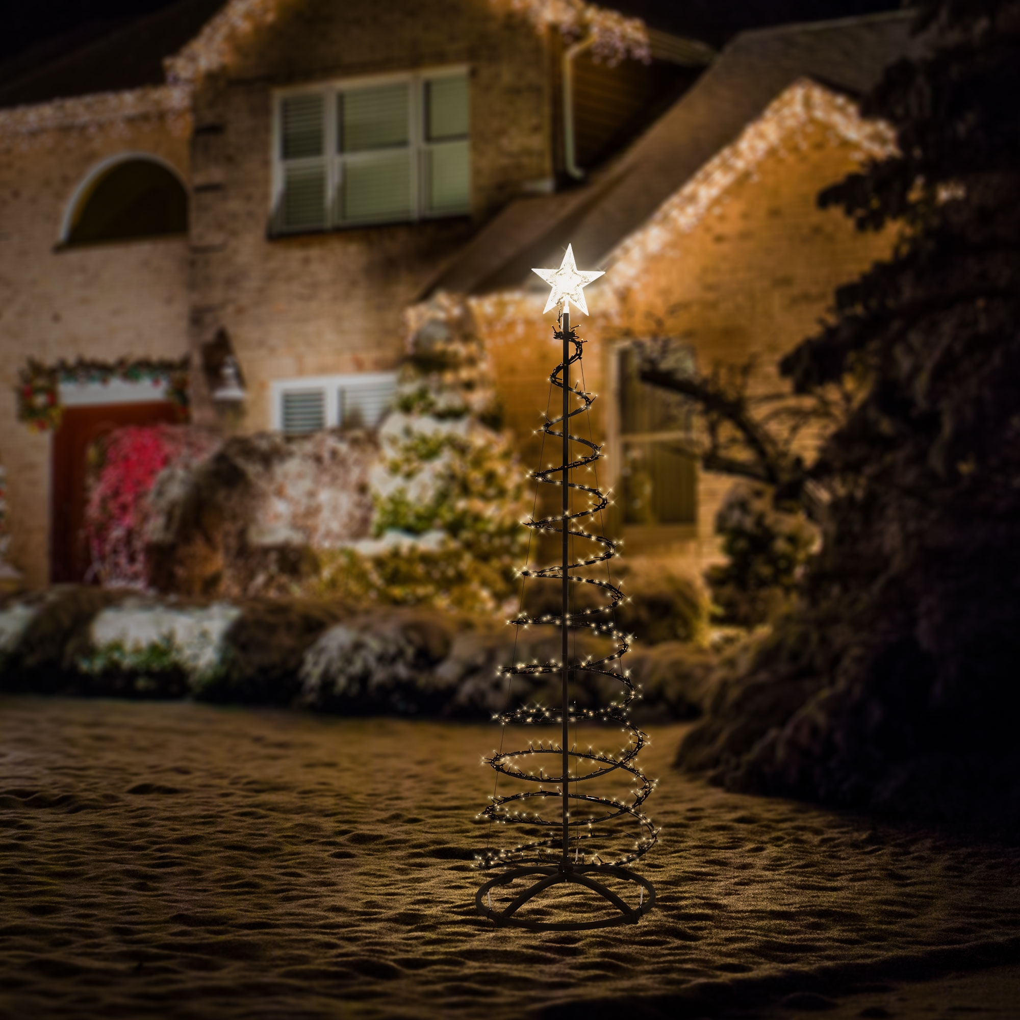 Beleuchteter kegelförmiger Weihnachtsbaum mit einem hellen Stern an der Spitze im Vorgarten vor einem Haus bei Nacht.