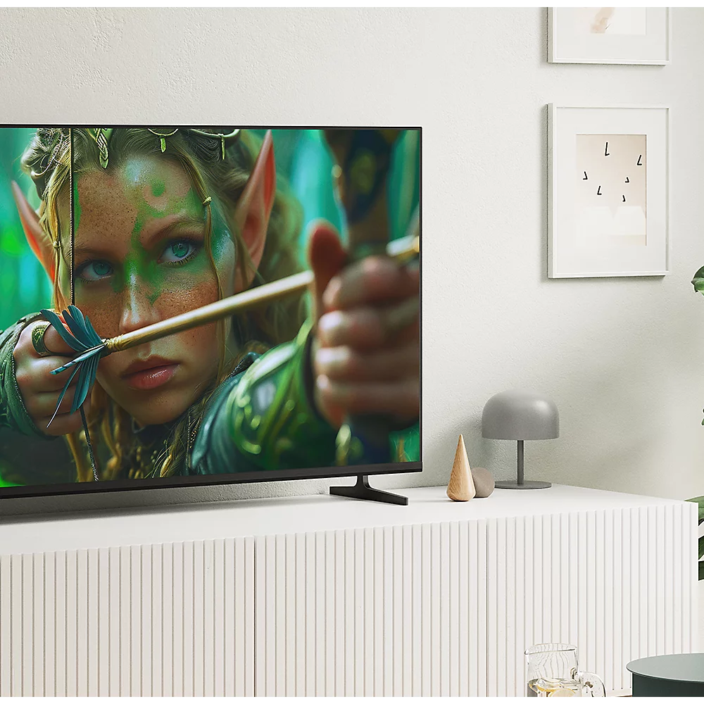 Ein Fernseher auf einem weißen Schrank zeigt eine Elfin mit Pfeil und Bogen, umgeben von gerahmten Bildern.