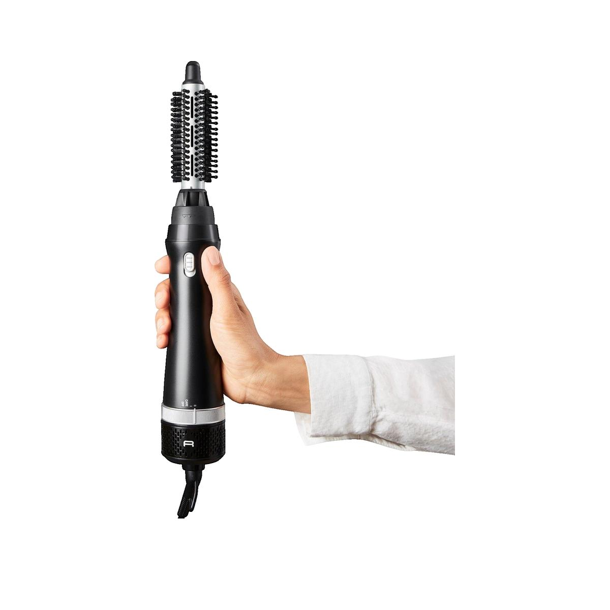 Una mano tiene una spazzola per capelli nera con accessorio su sfondo bianco.
